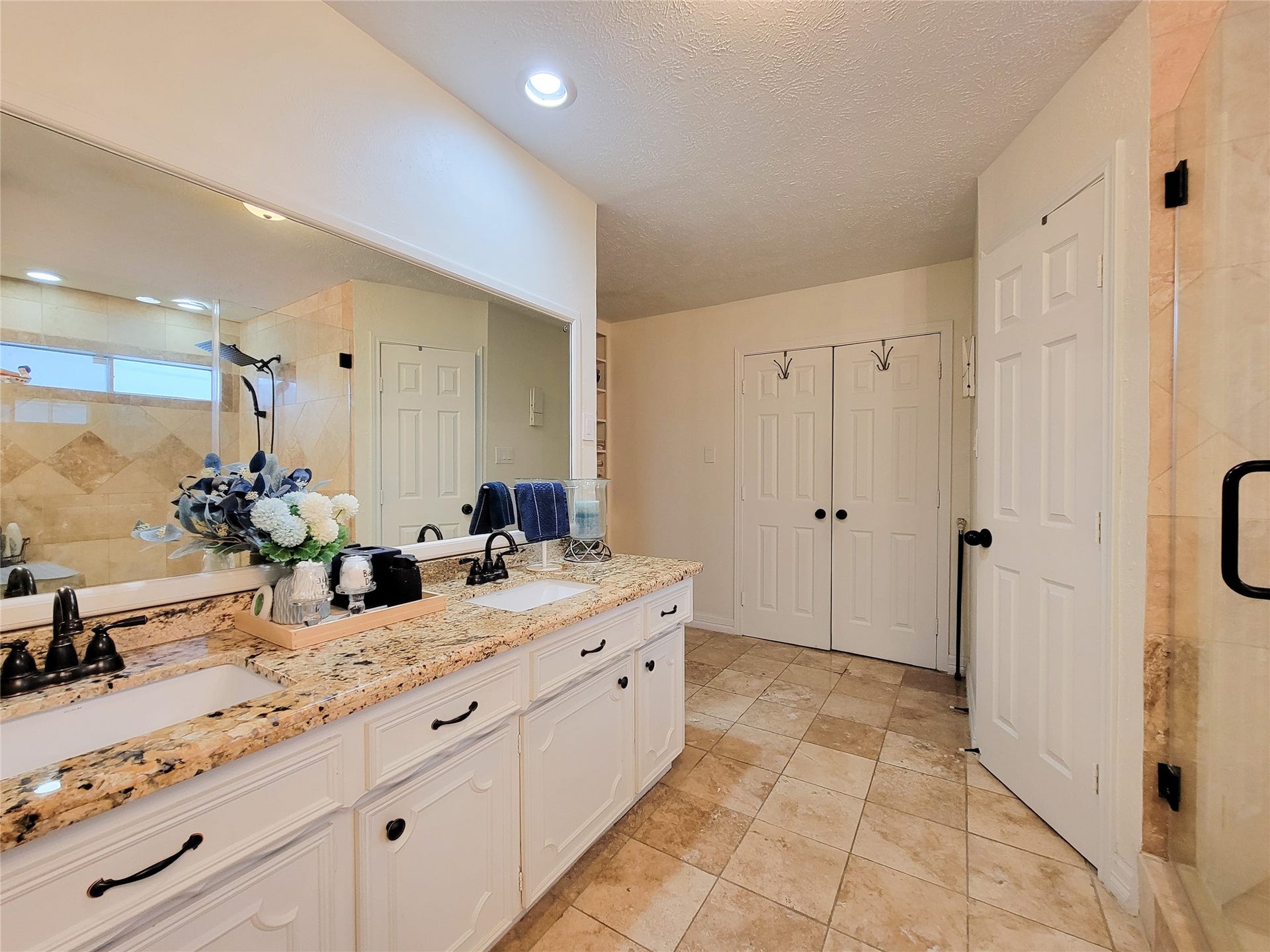 6235 Rolling Water Drive, Houston, TX 77069 This spacious bathroom features a dual-sink vanity with elegant granite countertops, ample storage, and a large mirror. It has a modern shower with glass doors, tiled flooring, and soft, neutral tones throughout, creating a serene atmosphere.