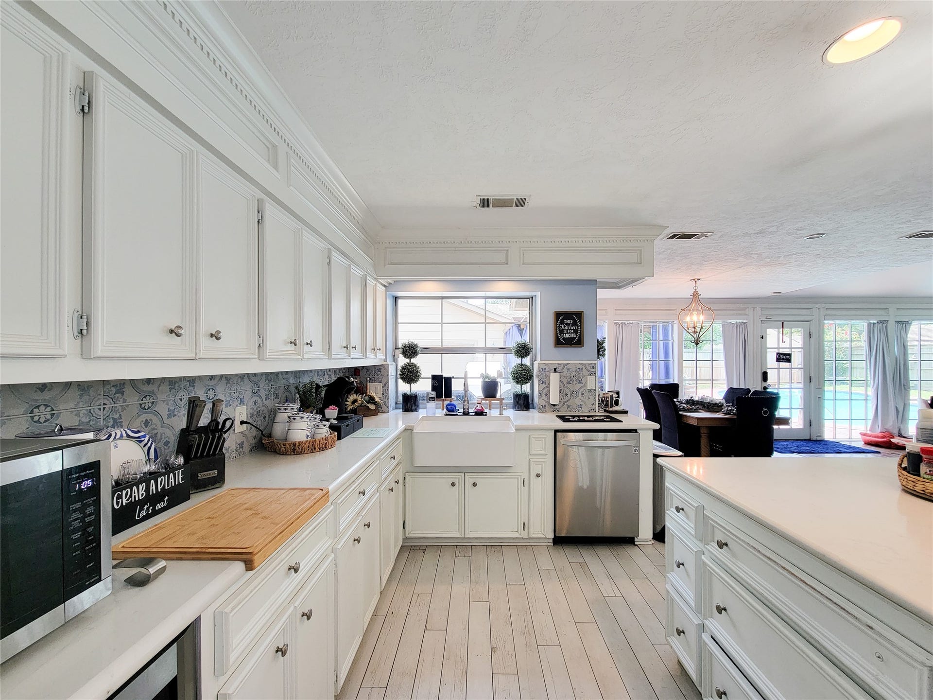 6235 Rolling Water Drive, Houston, TX 77069 Bright and spacious kitchen with elegant white cabinetry, a farmhouse sink, and modern appliances. The open layout flows into a dining area with large windows offering a view of the pool.