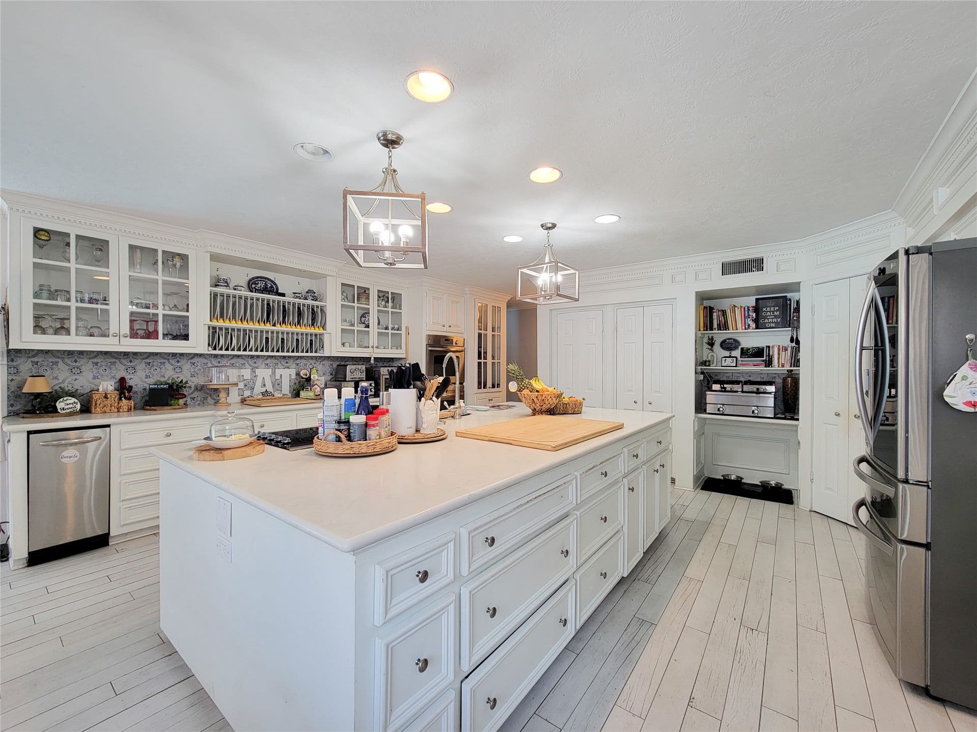 6235 Rolling Water Drive, Houston, TX 77069 This spacious kitchen features a large island with ample storage, modern stainless steel appliances, and elegant white cabinetry with glass fronts. The space is bright and inviting, enhanced by stylish pendant lighting and a sleek, open layout perfect for cooking and entertaining.