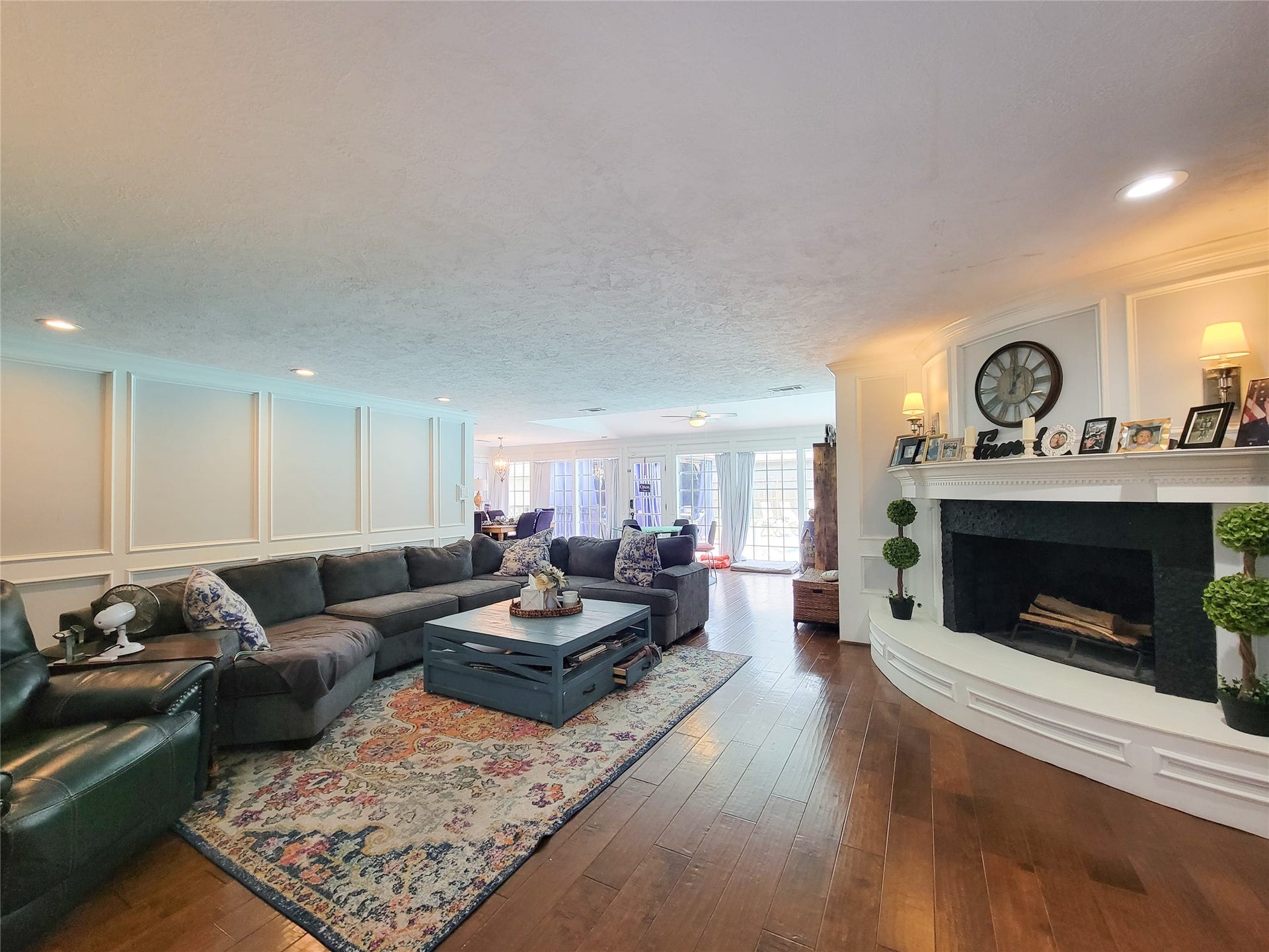 6235 Rolling Water Drive, Houston, TX 77069 This spacious living room features elegant wood flooring, a cozy fireplace with a decorative mantel, and ample natural light from large windows. The room is accented by a stylish sectional sofa and a large area rug, offering a warm and inviting atmosphere for relaxation and entertaining.