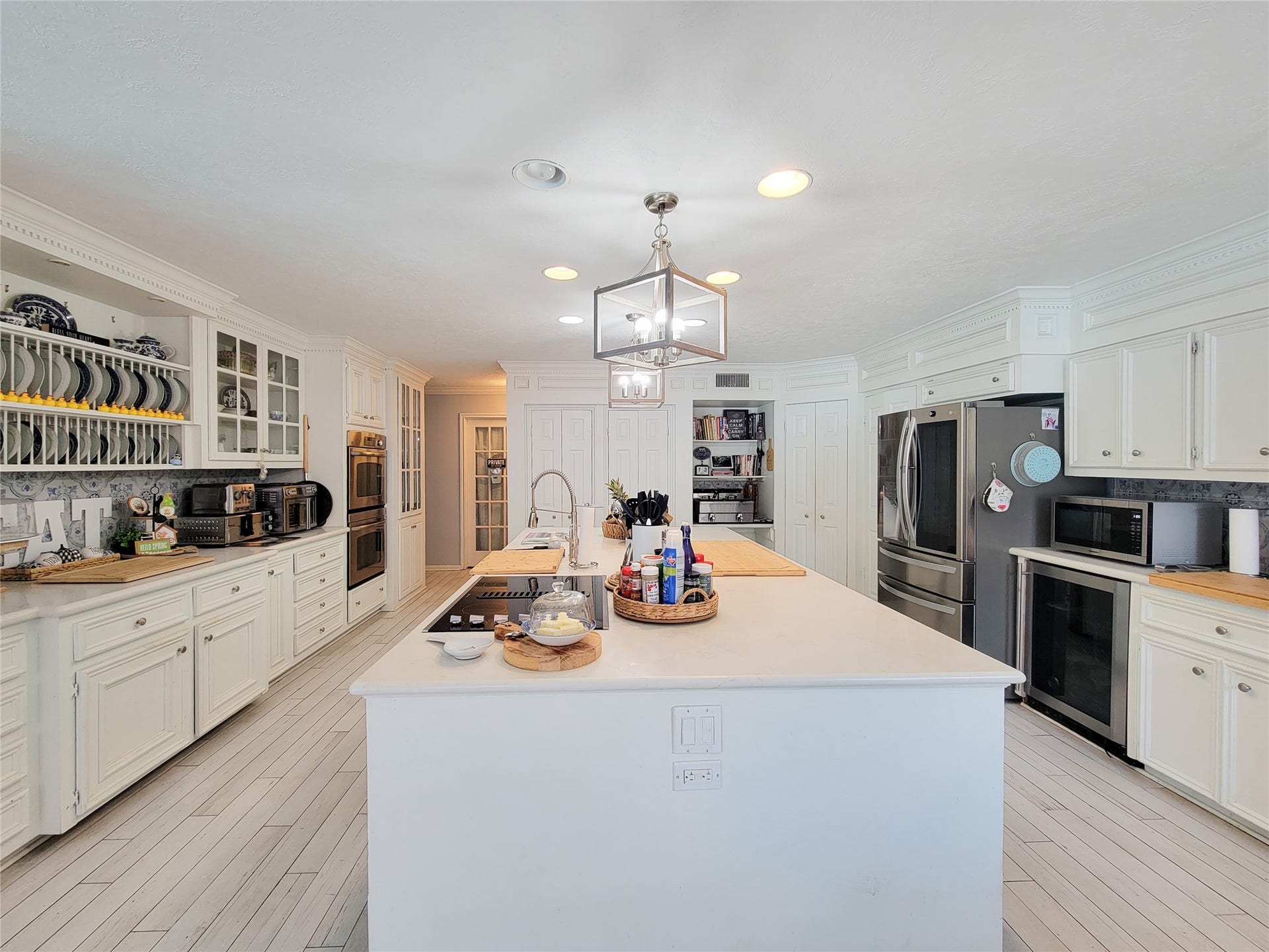 6235 Rolling Water Drive, Houston, TX 77069 This spacious kitchen features white cabinetry, modern stainless steel appliances, and a large central island with a built-in cooktop. The room is bright and inviting, with ample storage and elegant lighting, perfect for both cooking and entertaining.