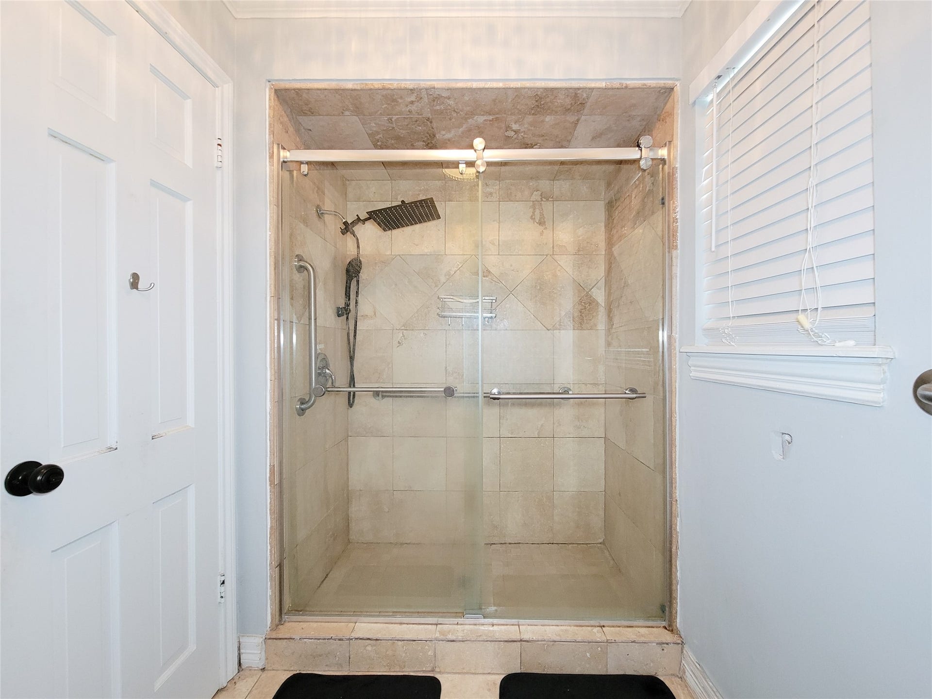 6235 Rolling Water Drive, Houston, TX 77069 This bathroom features a spacious walk-in shower with a glass door, tiled walls and ceiling, and a modern rainfall showerhead. It includes a built-in bench and grab bars for convenience, with a window providing natural light.
