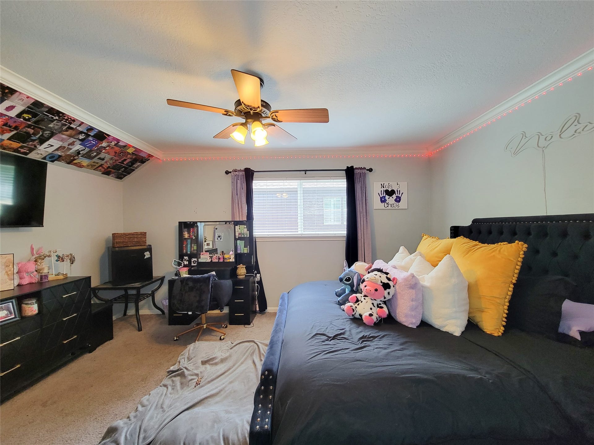 6235 Rolling Water Drive, Houston, TX 77069 This cozy bedroom features soft carpeting, a modern ceiling fan, and ample natural light from a large window. It includes a stylish bed setup with vibrant pillows, a workspace with a desk and chair, and a dresser for storage. Decorative lighting and personal touches add charm to the space.