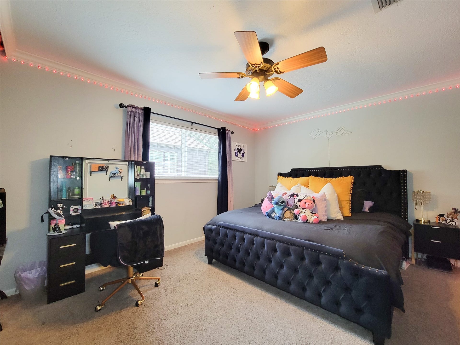 6235 Rolling Water Drive, Houston, TX 77069 Bright bedroom with a large window, ceiling fan, and cozy carpet. Features a stylish black bed with plush pillows and a charming vanity desk. Ideal for comfort and relaxation.