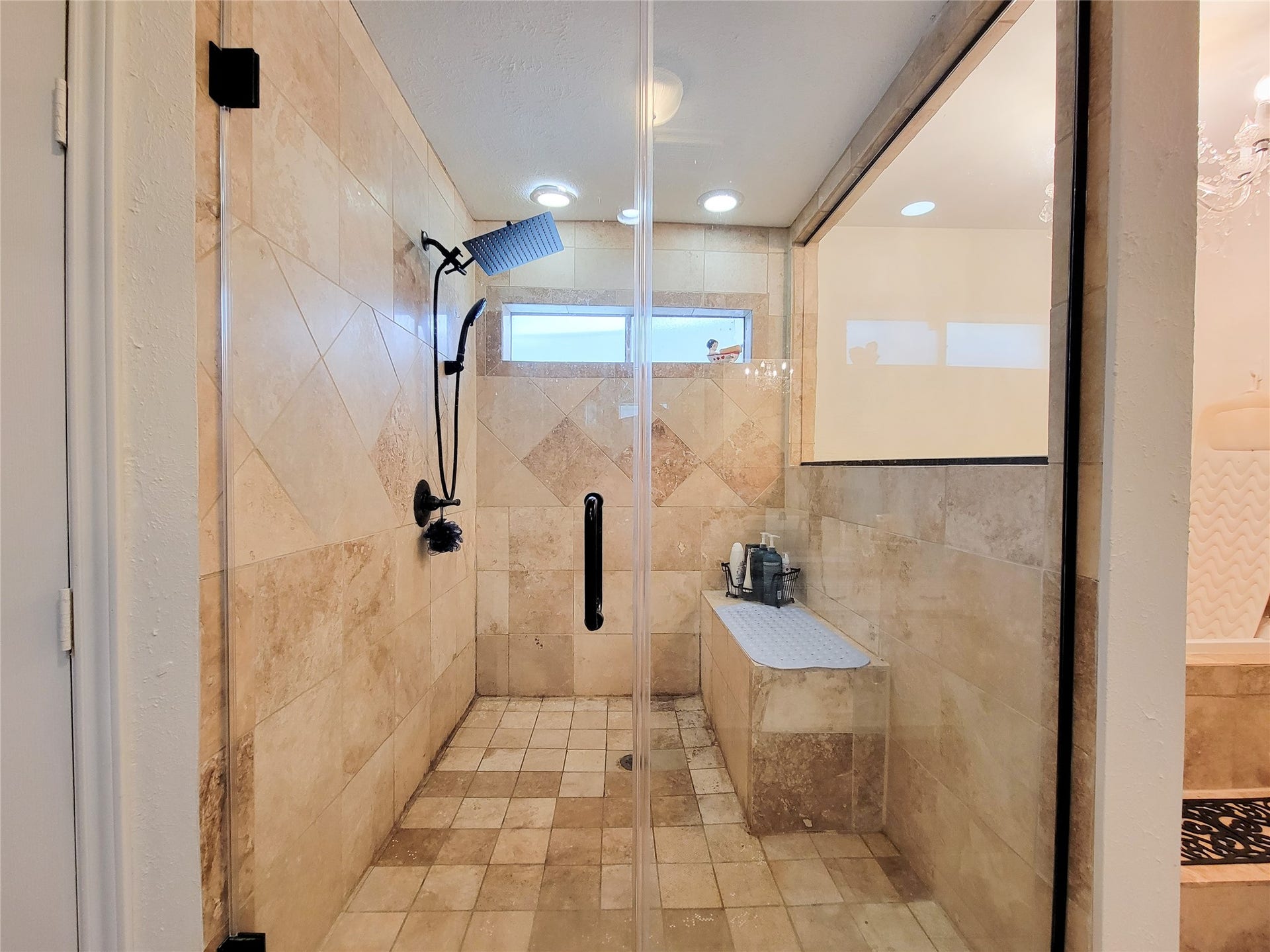 6235 Rolling Water Drive, Houston, TX 77069 This photo showcases a spacious walk-in shower with elegant beige tilework, a rainfall showerhead, and a built-in bench. The glass enclosure adds a modern touch, complemented by ample natural light from a small window.