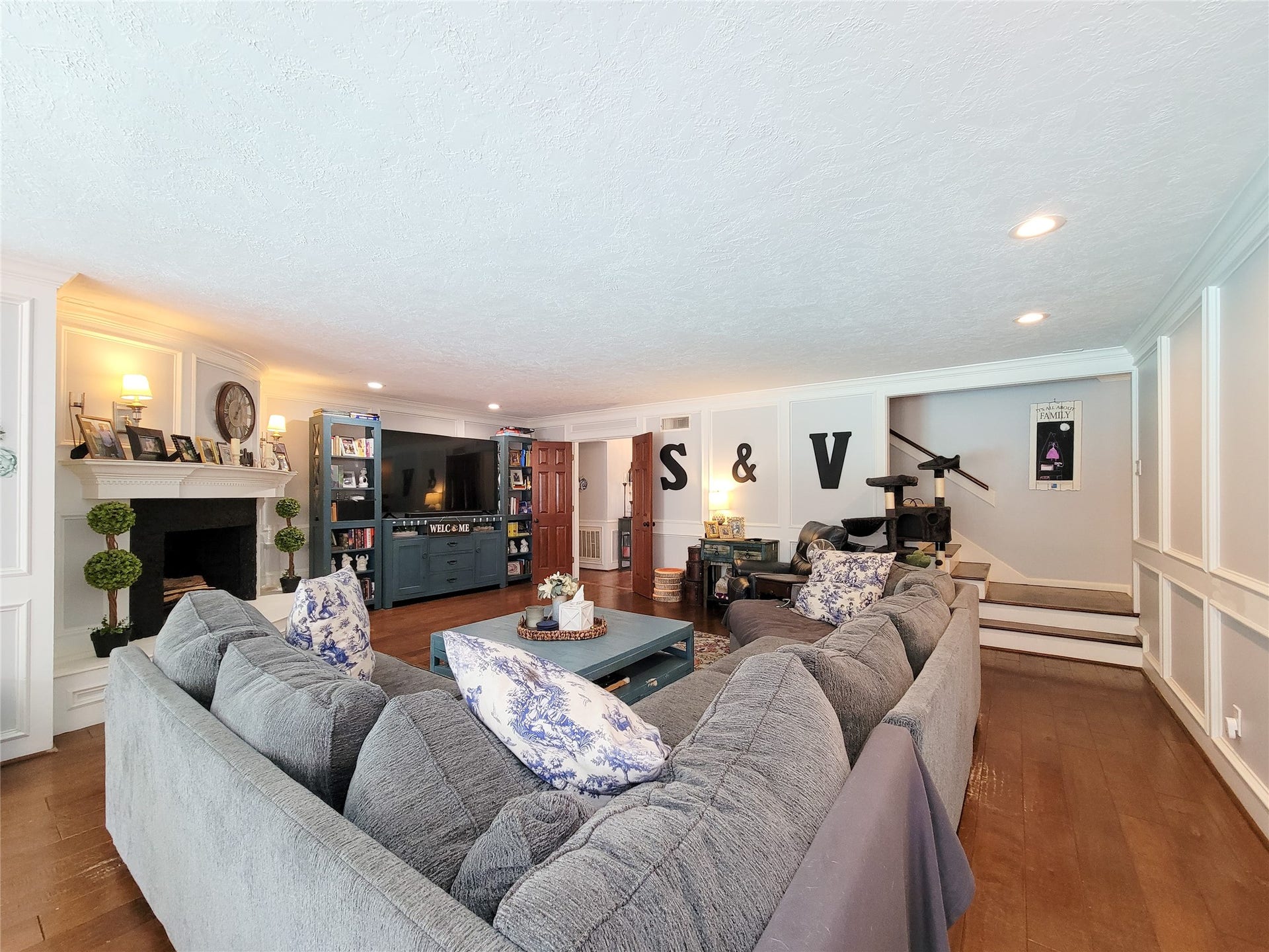 6235 Rolling Water Drive, Houston, TX 77069 This spacious living room features a cozy sectional sofa, a built-in fireplace, and elegant wood paneling. It includes ample shelving and a TV unit, creating a perfect blend of comfort and functionality.