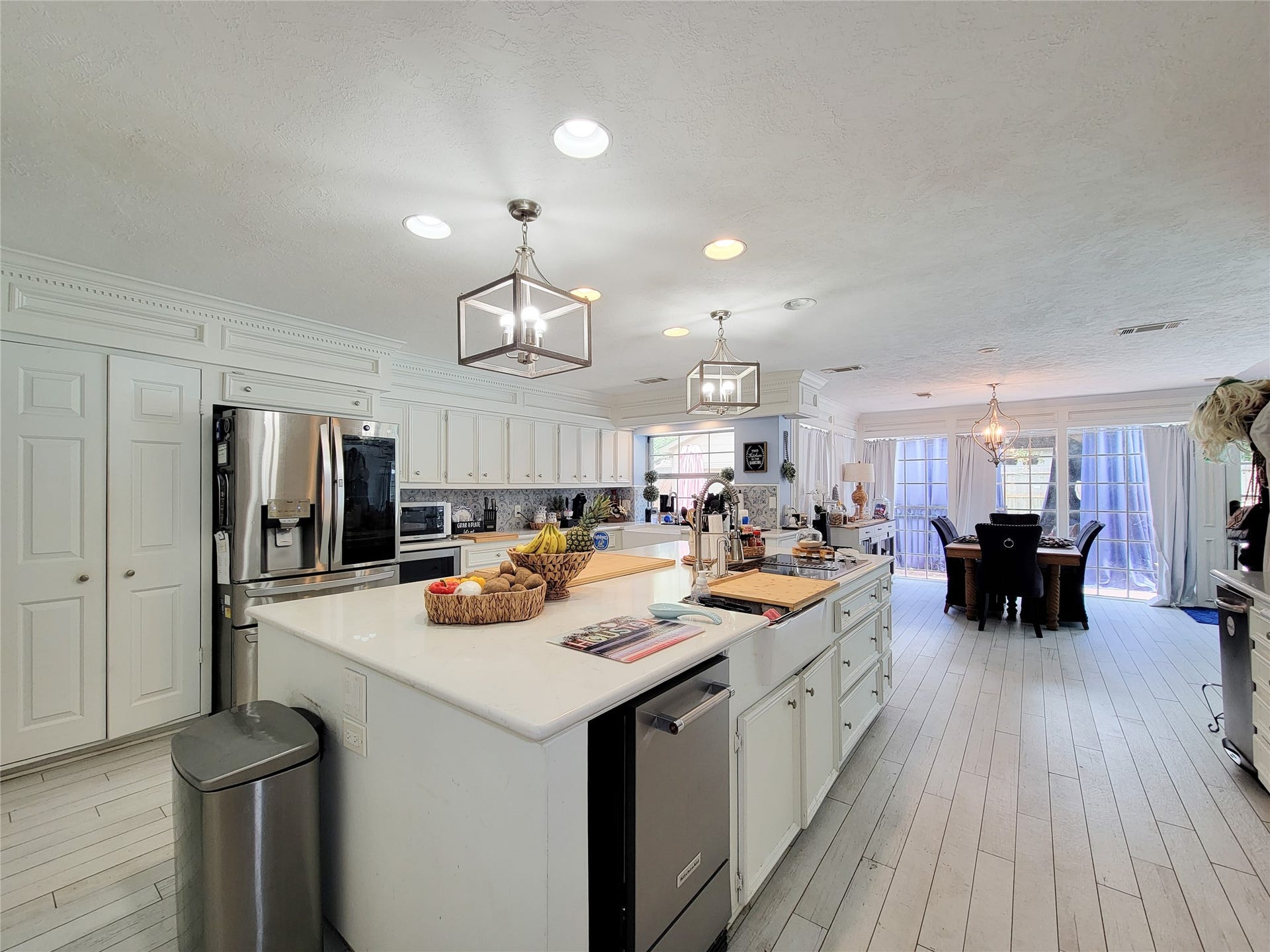 6235 Rolling Water Drive, Houston, TX 77069 This kitchen features a spacious, open layout with modern stainless steel appliances and a large central island. It has ample white cabinetry, hardwood floors, and recessed lighting. The adjoining dining area is bright, thanks to large windows and glass doors leading outside.