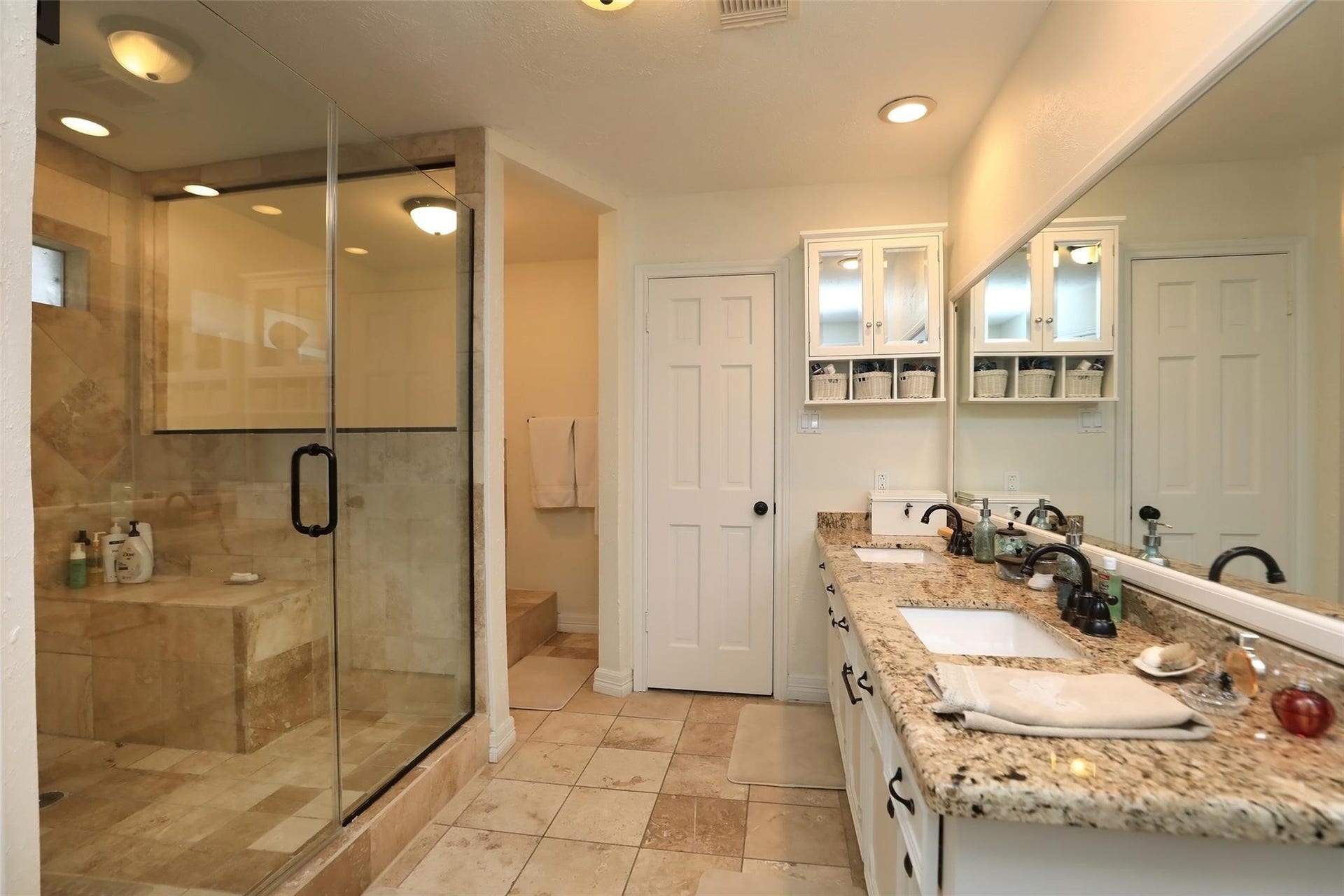 6235 Rolling Water Drive, Houston, TX 77069 This bathroom features a spacious walk-in glass shower with elegant tile work, dual sinks with granite countertops, and ample storage. It offers a clean, modern aesthetic with warm lighting.