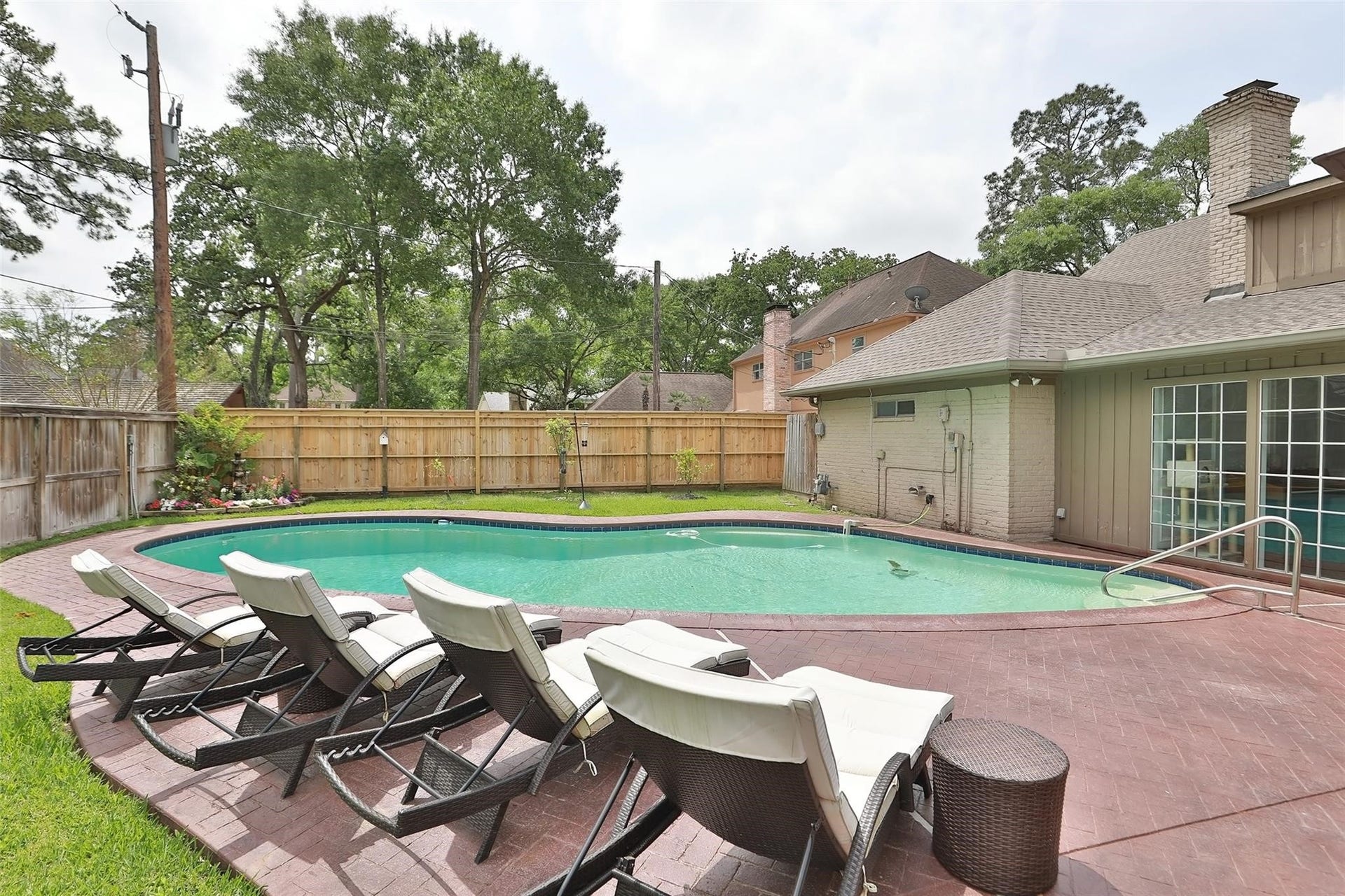 6235 Rolling Water Drive, Houston, TX 77069 Photo showcases a backyard with a swimming pool surrounded by a brick patio. There are several lounge chairs for relaxation and the area is enclosed by a wooden fence, providing privacy. Mature trees in the background offer shade and a serene atmosphere.