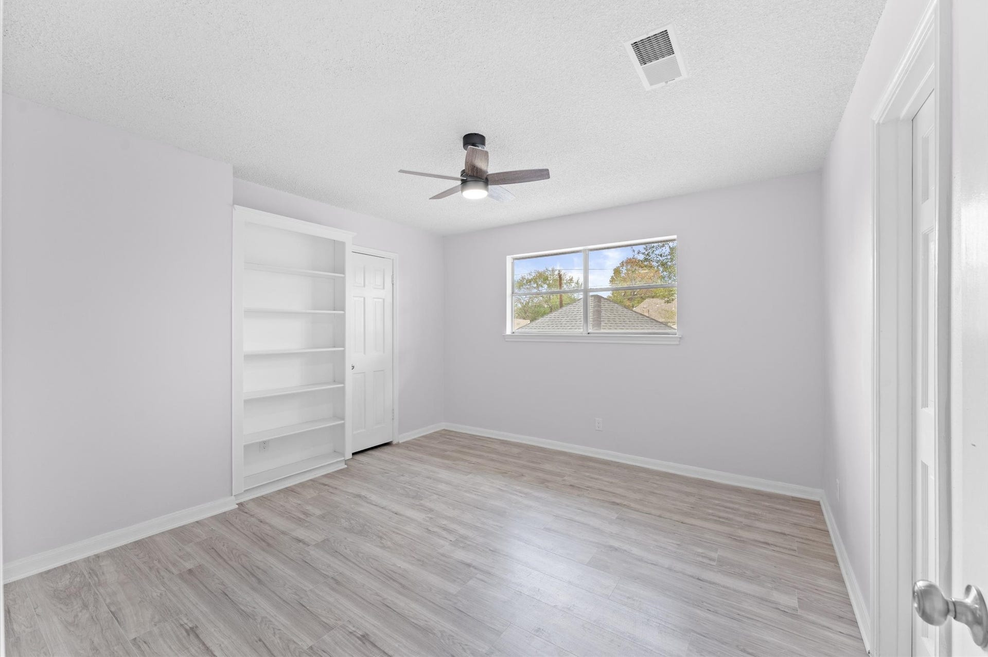 This home provides three secondary bedrooms in addition to the primary suite. Enjoy this view of Bedroom 2 with wood-like laminate flooring, a spacious closet, and a convenient built-in bookshelf.