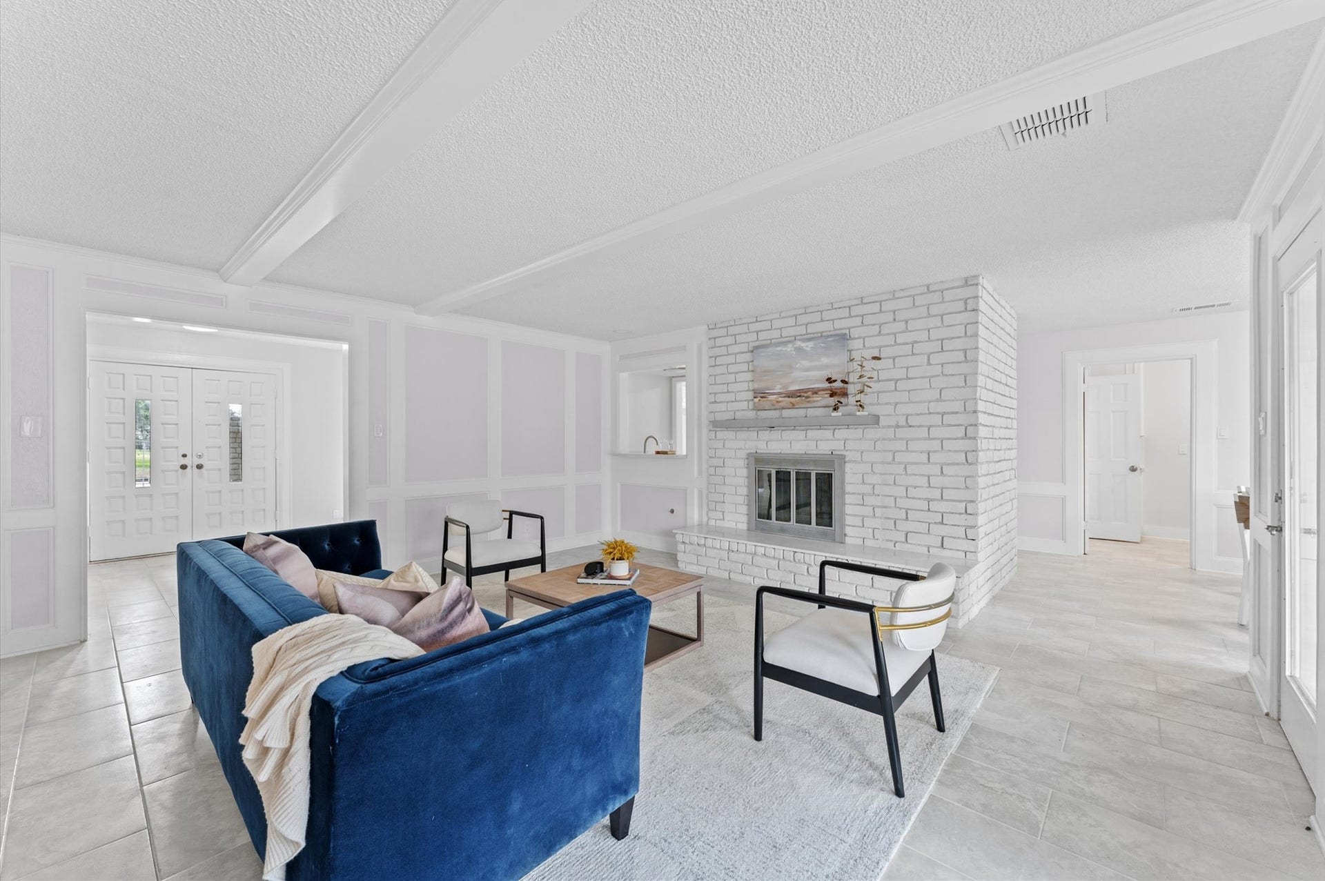 A comfortable, spacious living room features stylish wainscoting and a classic brick fireplace and hearth. Wide entrances to the room create a welcoming vibe.