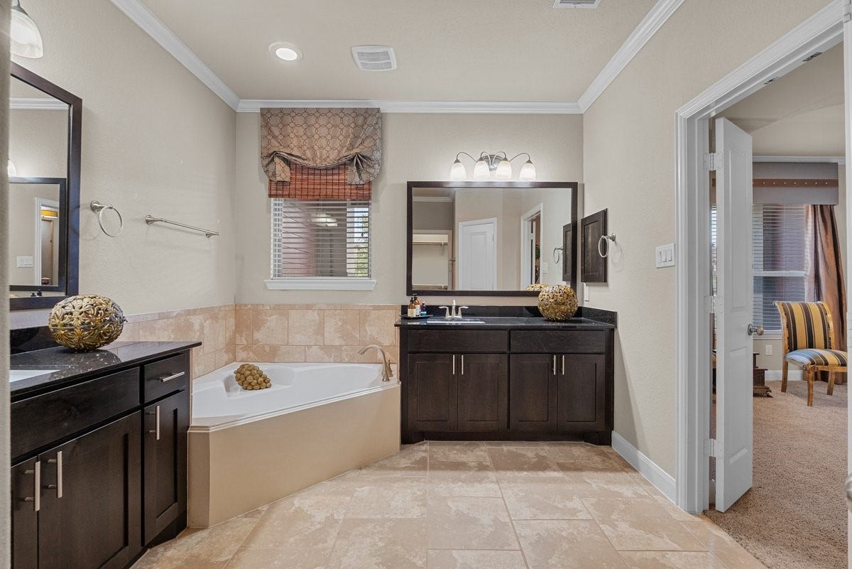416 Via Regatta Drive, Webster, TX 77598 A deep corner soaking tub sits beneath a bright window, providing the perfect place to unwind, while the separate, grand walk-in shower features an architectural stone archway and floor-to-ceiling custom tilework.