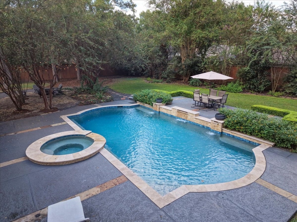 14026 Champions Hamlet Court, Houston, TX 77069 A raised concrete seating area beside the pool, framed by manicured hedges, is made for outdoor dining and lounging, with mature crape myrtles and trees for shade and privacy.