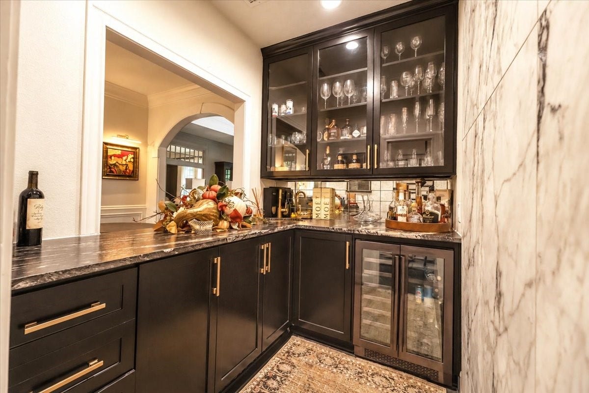 14026 Champions Hamlet Court, Houston, TX 77069 Custom cabinetry with glass fronts, a gold sink, and a leathered-granite waterfall countertop make hosting easy, with a wine fridge beneath for chilled bottles.