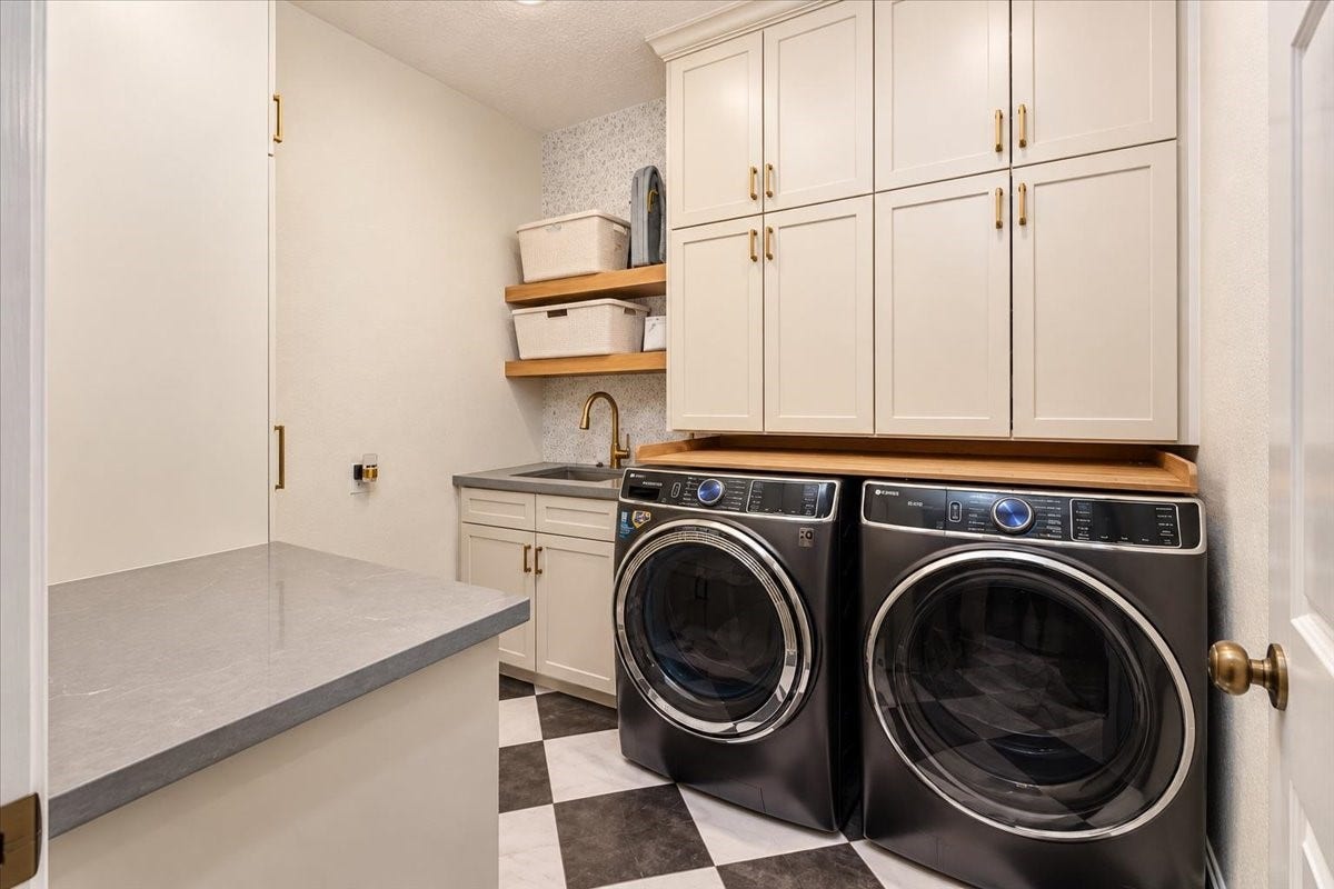 14026 Champions Hamlet Court, Houston, TX 77069 Custom cabinetry with gold hardware, open wood shelves, and a sink with a gold sprayer faucet give this laundry room room for supplies, folding, and everyday routines.