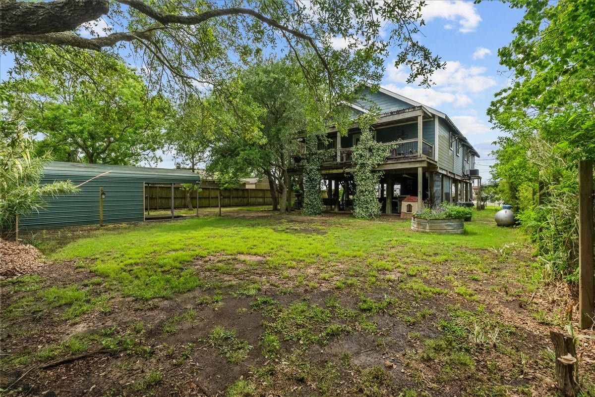 939 17th Street, Dickinson, TX 77539 Spacious backyard with mature trees, multiple storage structures and a view of the home's elevated design and covered outdoor areas