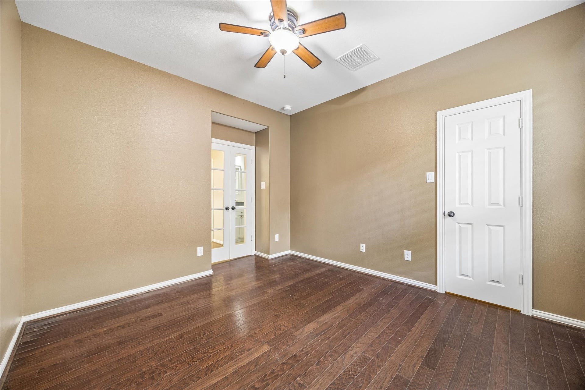 Versatile first-floor study or bedroom featuring wood flooring, double French doors and a ceiling fan, offering flexibility for a home office, guest accommodations or nursery.