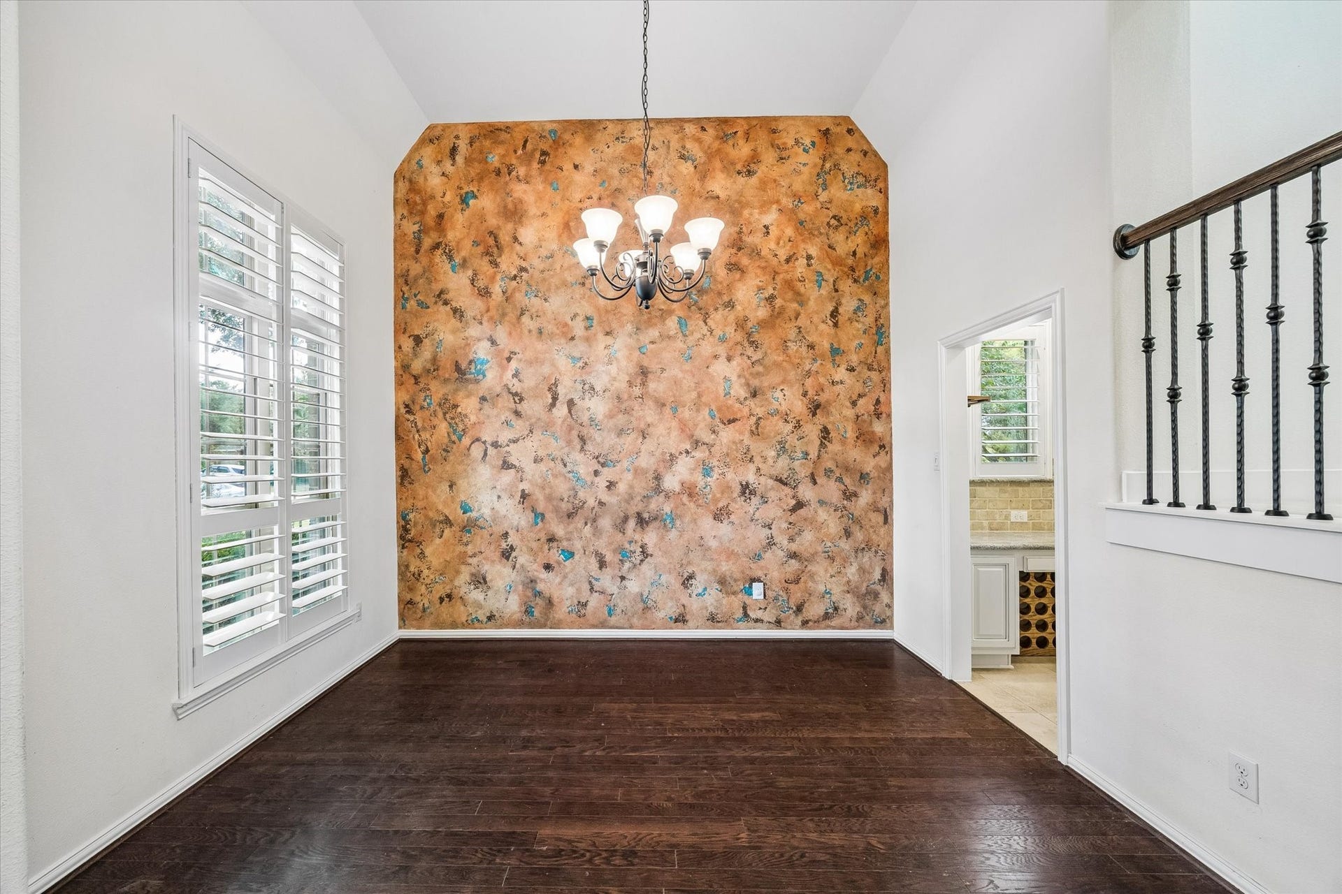 Plantation shutters filter natural light into the dining room, where a high ceiling, wood flooring, and a decorative accent wall provide an inviting setting for gatherings.