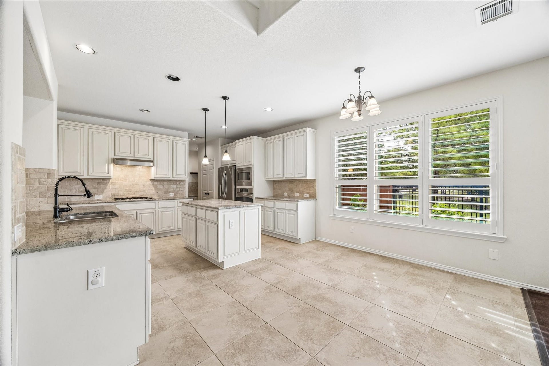 Island kitchen offers abundant white cabinetry, generous counter space and pendant lighting. Adjoining  breakfast area with plantation shutters provides a bright setting for casual dining.