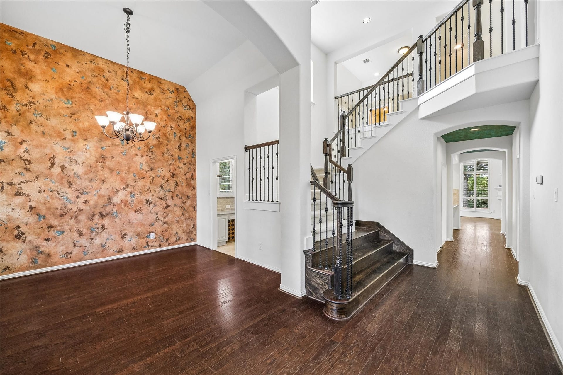 The formal dining area features rich wood flooring, a chandelier and a warm-toned accent wall. Two-story foyer showcases the sweeping staircase and iron balusters.