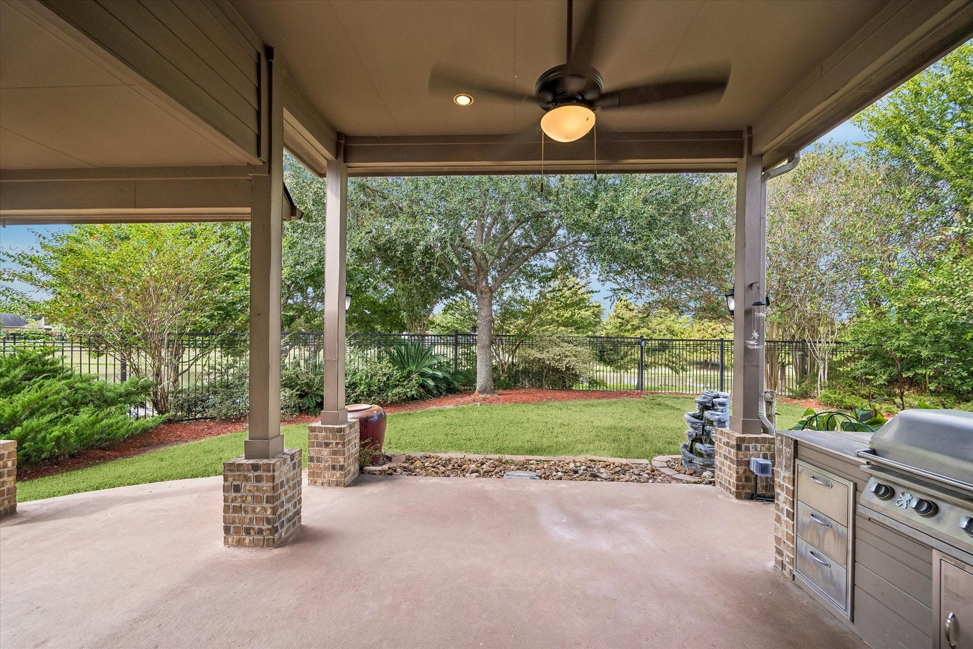 Spacious covered patio features a built-in grill, ceiling fan and brick-accented columns, with room for outdoor dining and lounging overlooking the landscaped backyard and lake.