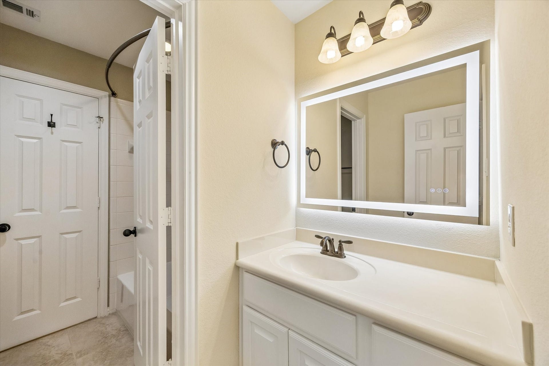 This Jack-and-Jill bath connects two bedrooms and features a white vanity with generous counter space, bronze-tone fixtures, and an illuminated mirror.