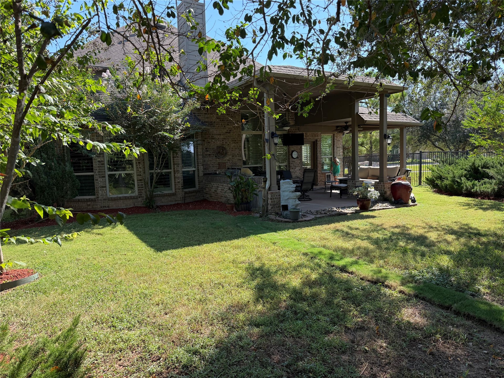A spacious covered patio overlooks the backyard, offering a shaded spot for outdoor dining and relaxing, with an open lawn for established trees completing the setting.