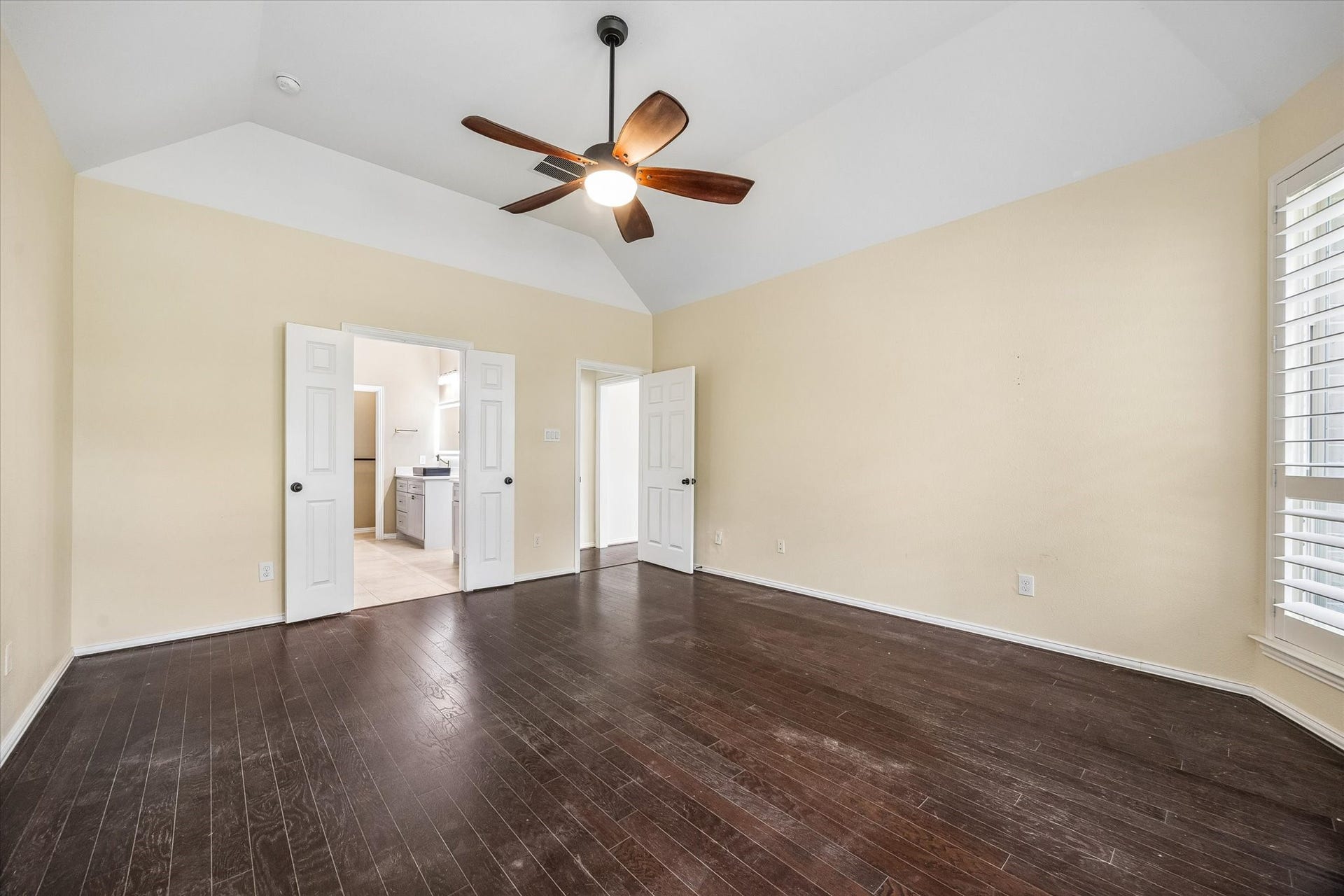 Alternate view of the primary bedroom highlights its generous proportions and vaulted ceiling, with double doors opening to the en-suite bath.