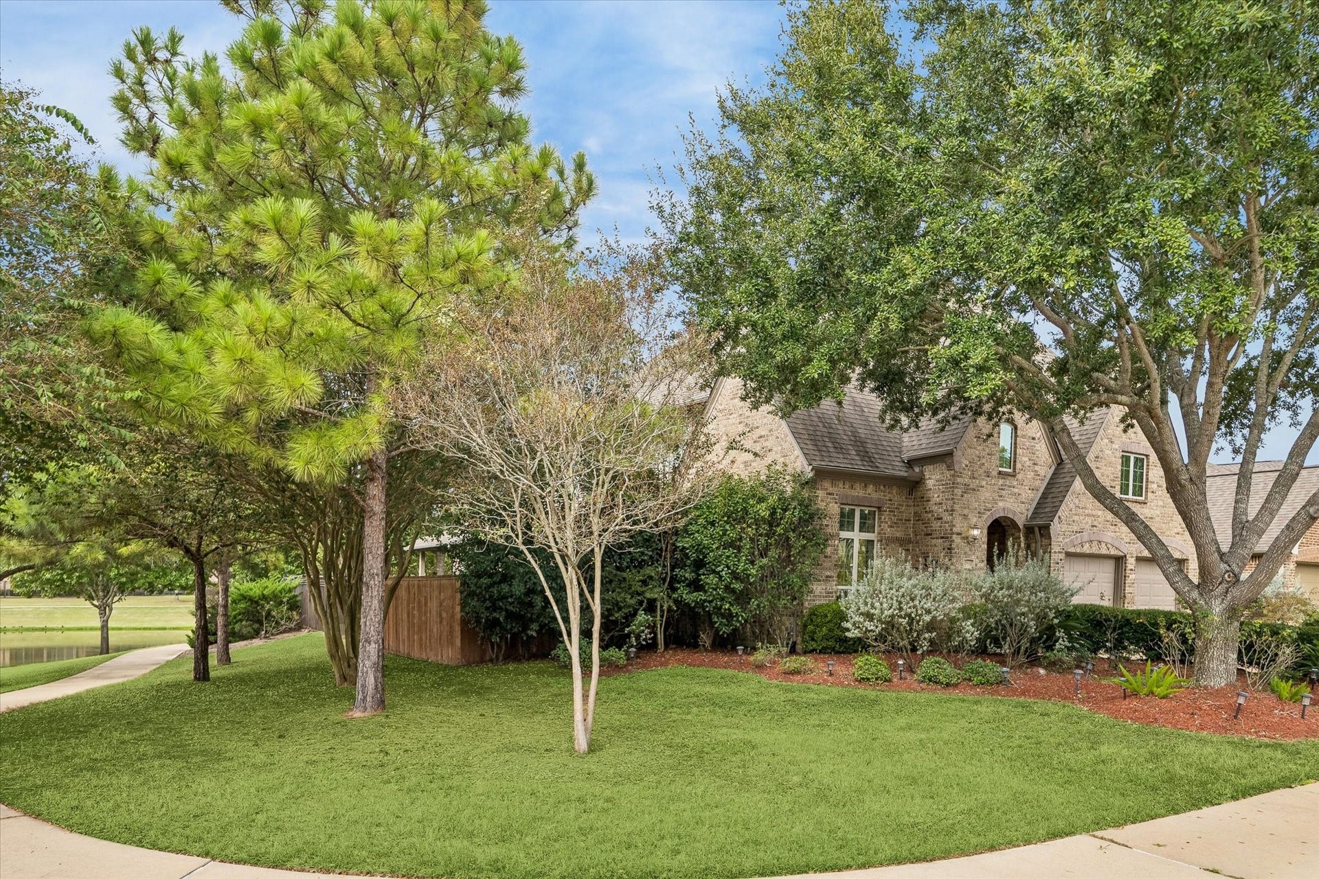 Side view highlights the home's tree-lined setting, with adjacent green space and views of the lake beyond.