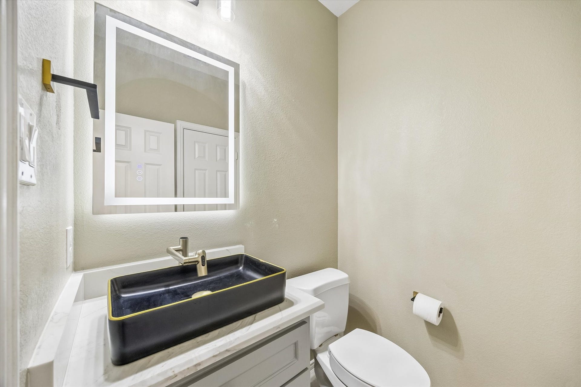 The first-floor guest powder room features a string rectangular vessel sink, an illuminated mirror and vanity with storage, combining distinctive style with everyday convenience.