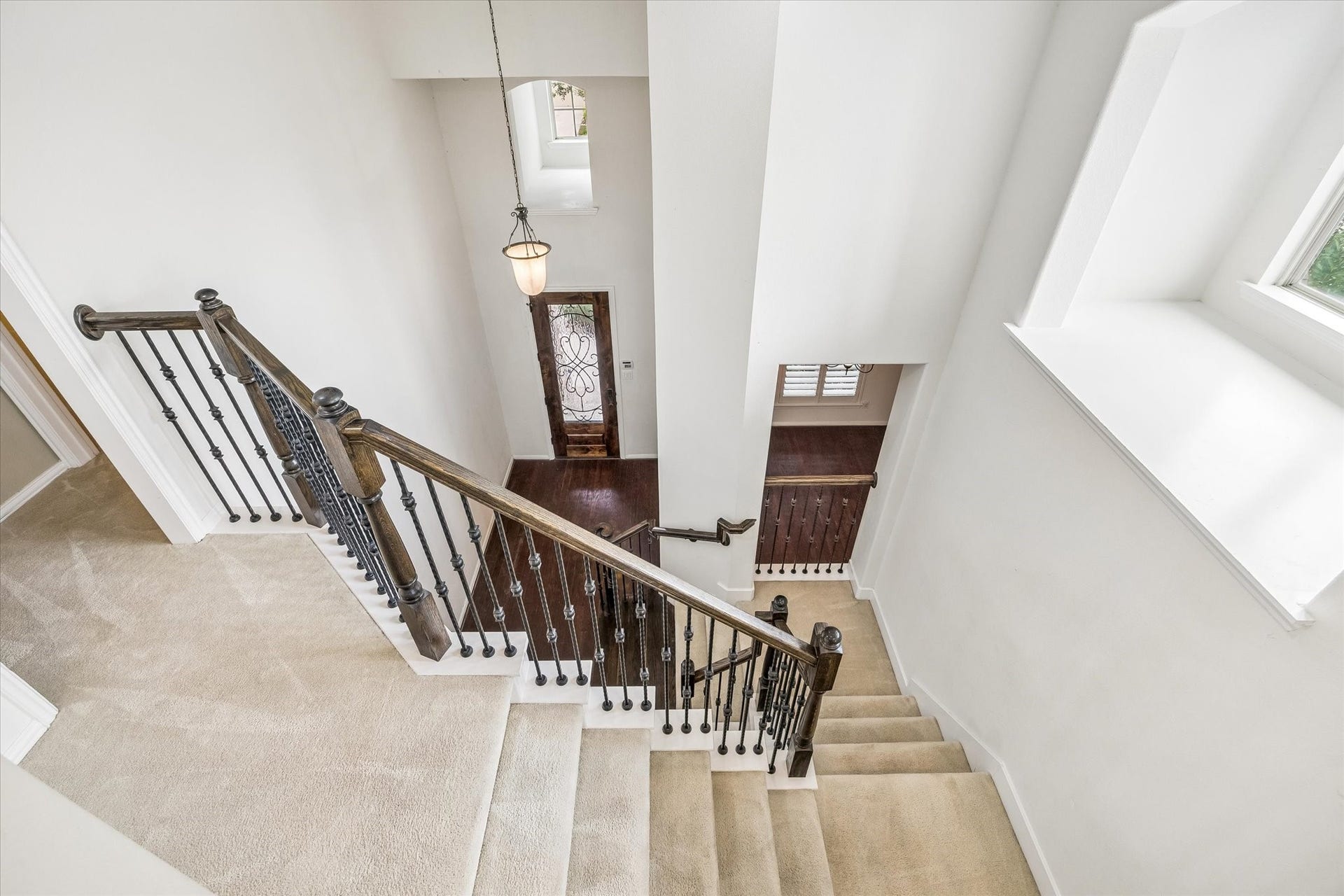 View from the upstairs landing highlights the staircase's wood handrails and decorative metal balusters, with the two-story foyer and leaded glass front door.