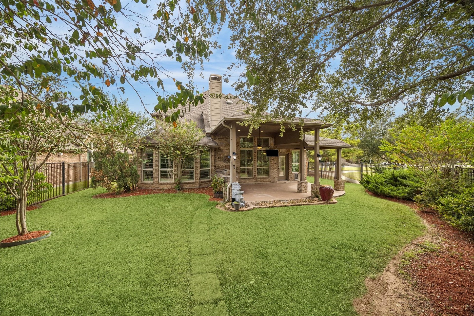 A touch of country living, with leafy tres, lush greenery, and an open lawn creating a natural retreat just beyond the covered patio.