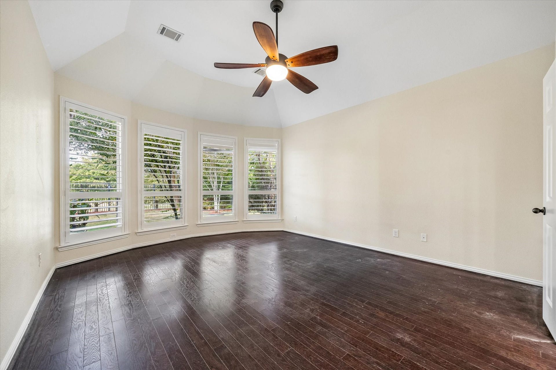 Spacious primary bedroom features a bay of tall windows, framing beautiful lake views. Plantation shutters, rich wood flooring and a vaulted ceiling complete this inviting retreat.