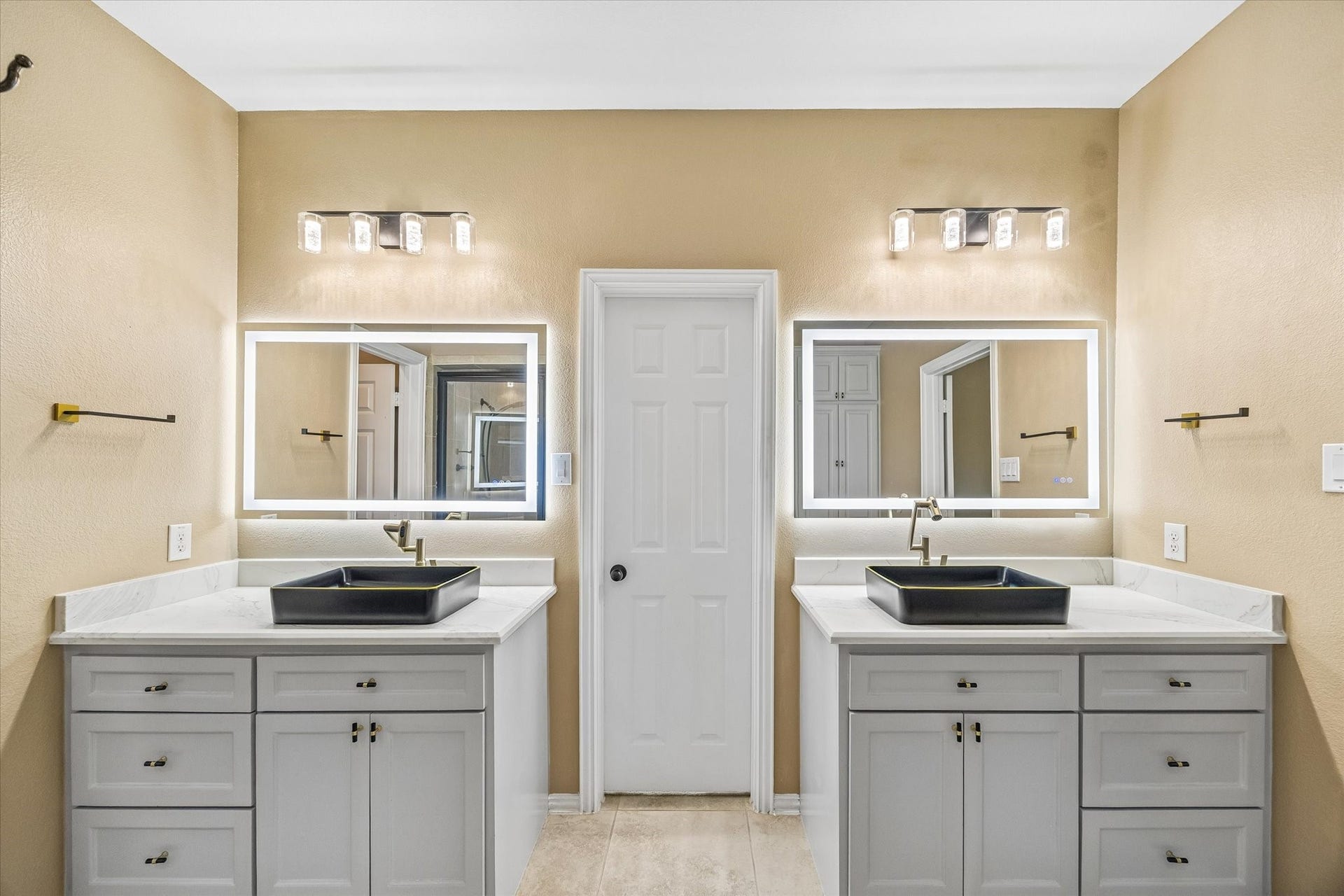 Separate vanities offer individual space, each with a rectangular vessel sink, illuminated mirror and generous drawer and cabinet storage.