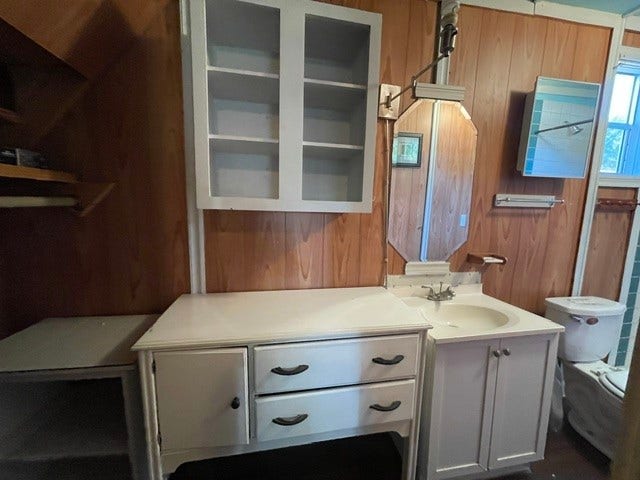 408 B Vista Road, Pasadena, TX 77504 Charming bathroom with wood-paneled walls, featuring a spacious white vanity with ample storage and an mirror, offering a cozy and functional space.