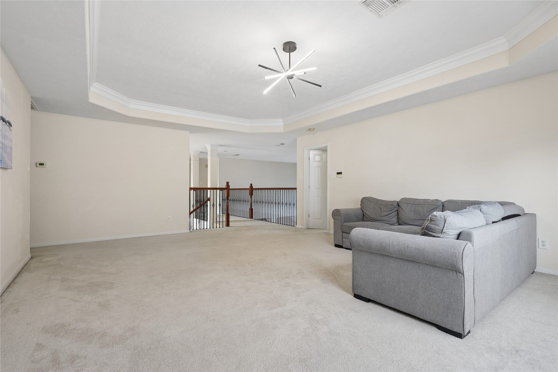 2614 Sunset Lake Drive, Sugar Land, TX 77478 Spacious, carpeted upstairs living area with neutral tones, featuring a modern ceiling light fixture and a cozy gray sectional sofa. The room opens to a railing overlooking the staircase, adding an airy feel. Ideal for relaxation or entertaining.