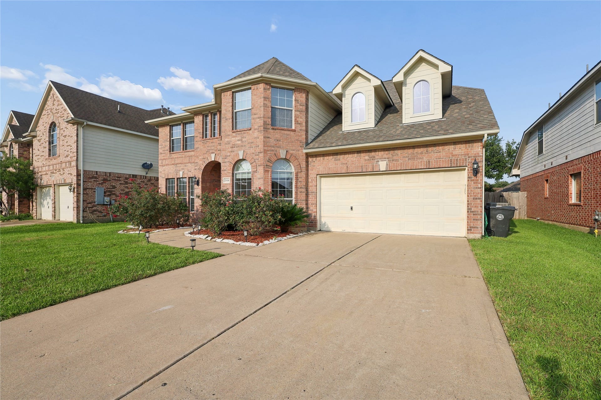 2614 Sunset Lake Drive, Sugar Land, TX 77478 This photo showcases a two-story brick home with a well-maintained lawn, a double garage, and charming dormer windows. The driveway is spacious, and the front garden features attractive landscaping. Perfect for a family seeking a suburban setting.
