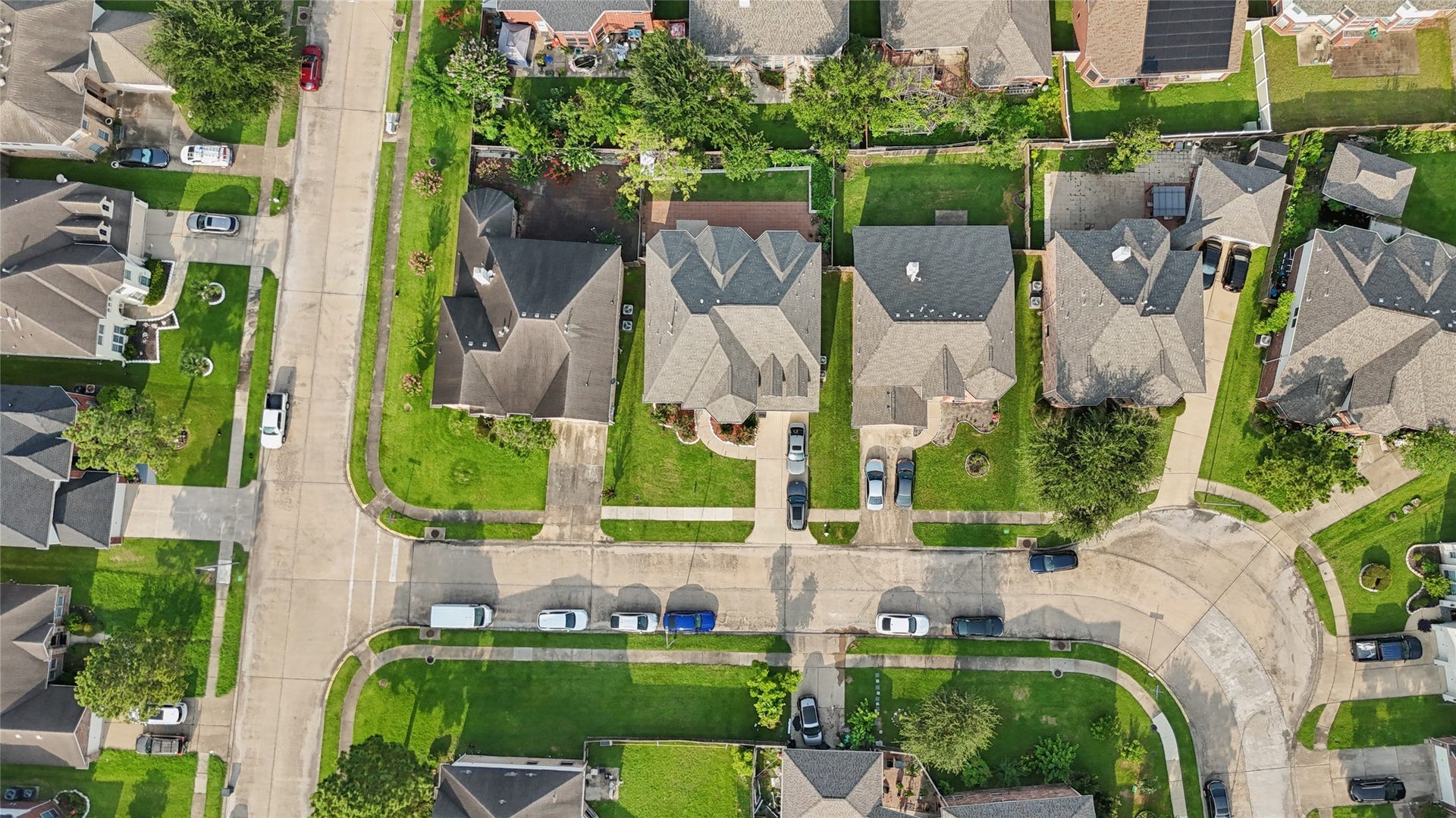 2614 Sunset Lake Drive, Sugar Land, TX 77478 This aerial view showcases a suburban neighborhood with well-maintained homes, neatly landscaped yards, and a curving street layout. The area appears peaceful and residential, with ample parking and green spaces.