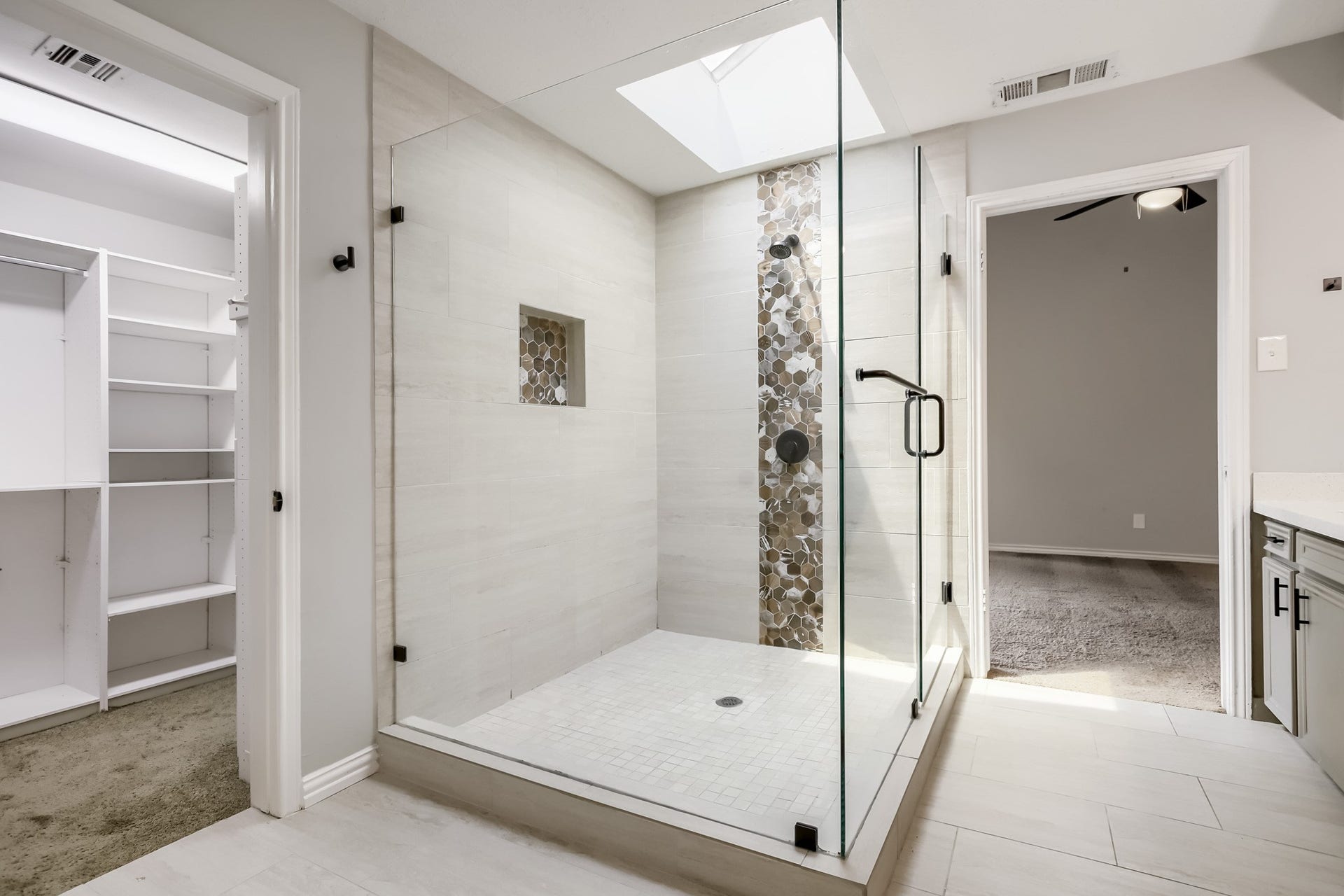 16505 Cornwall Street, Jersey Village, TX 77040 Modern bathroom featuring a spacious glass-enclosed shower with stylish tile accents and a skylight for natural light. Adjacent to a walk-in closet, offering convenience and ample storage.