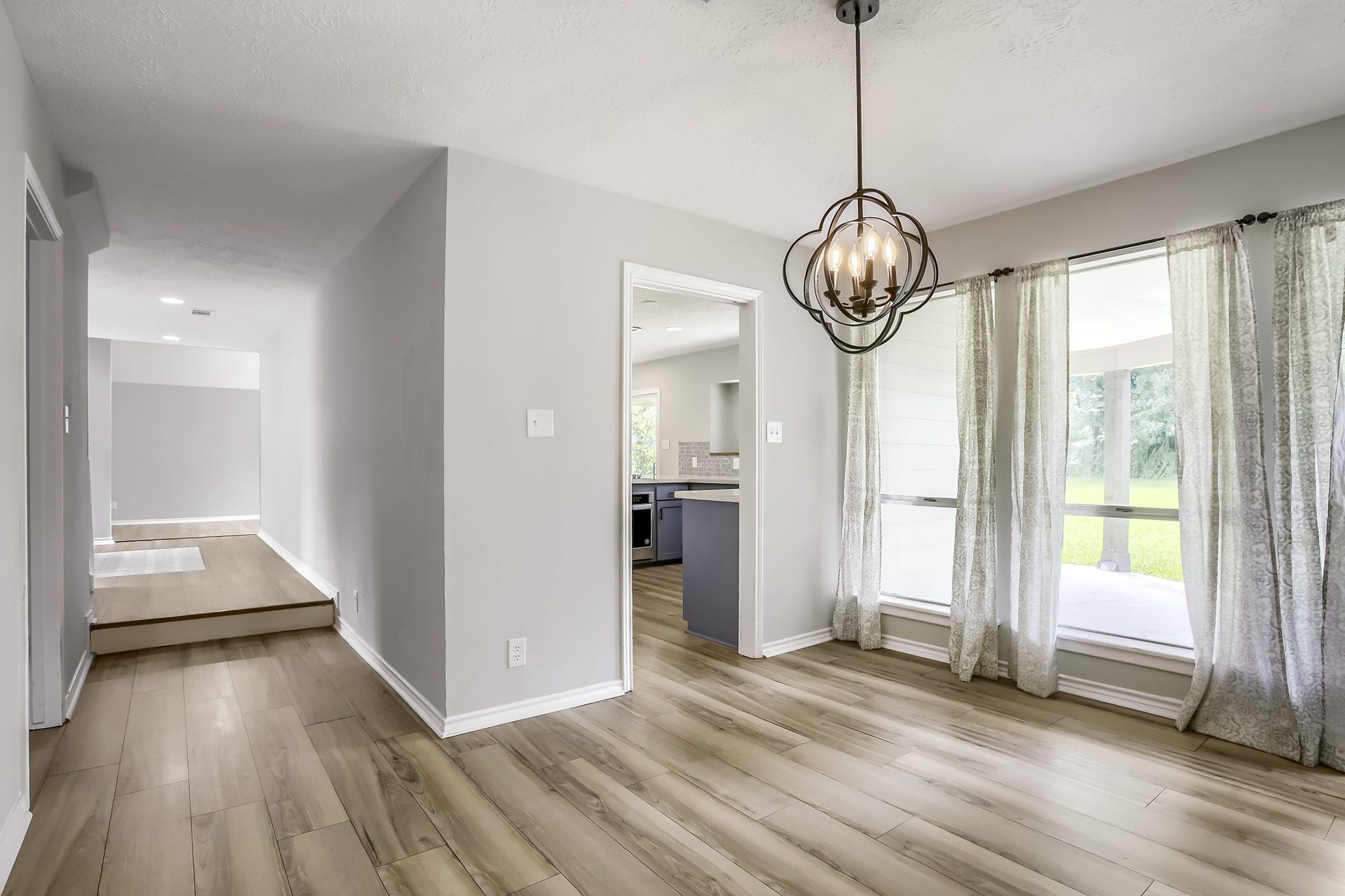 16505 Cornwall Street, Jersey Village, TX 77040 This home features a bright, open space with modern light wood flooring and large windows offering plenty of natural light. The elegant chandelier and neutral color palette create a welcoming atmosphere, with a view into the kitchen and access to the outdoor area.
