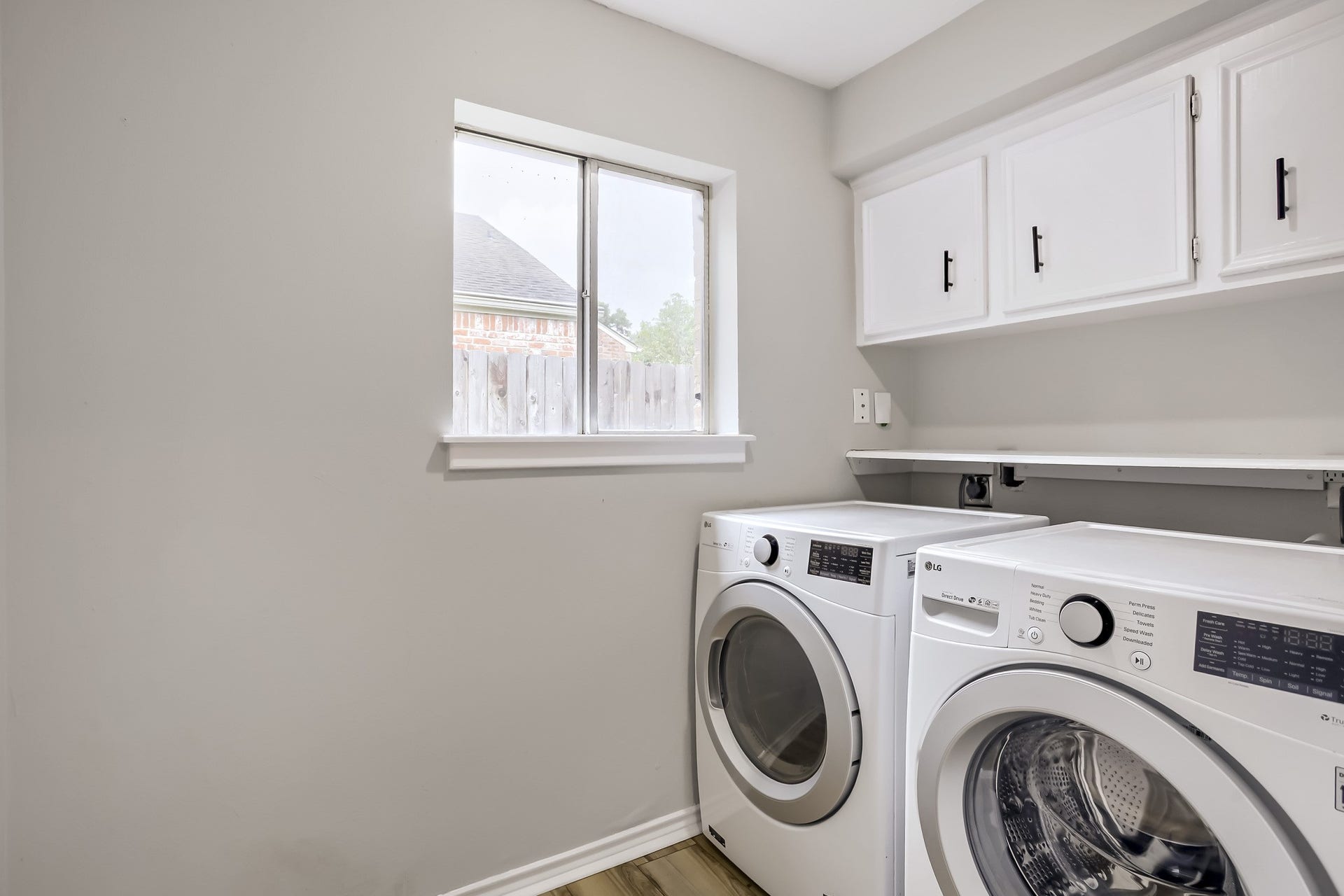 16505 Cornwall Street, Jersey Village, TX 77040 This laundry room features modern appliances, a window for natural light, and upper cabinets for storage. The neutral color scheme and wood-style flooring create a clean, functional space.