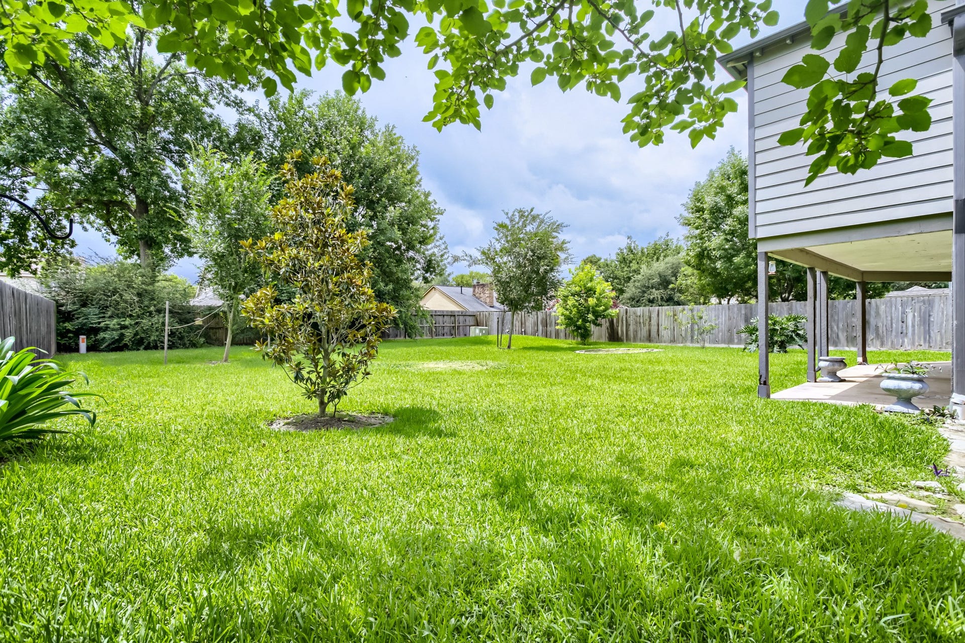 16505 Cornwall Street, Jersey Village, TX 77040 A different view of the spacious backyard featuring lush green grass, several small trees, and a fenced perimeter. The area provides ample outdoor space perfect for relaxation or entertainment.