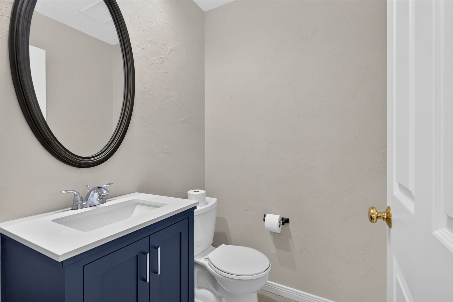 A stylish navy vanity, modern fixtures, and a circular mirror add personality to this conveniently located half bath while keeping the space polished and functional.