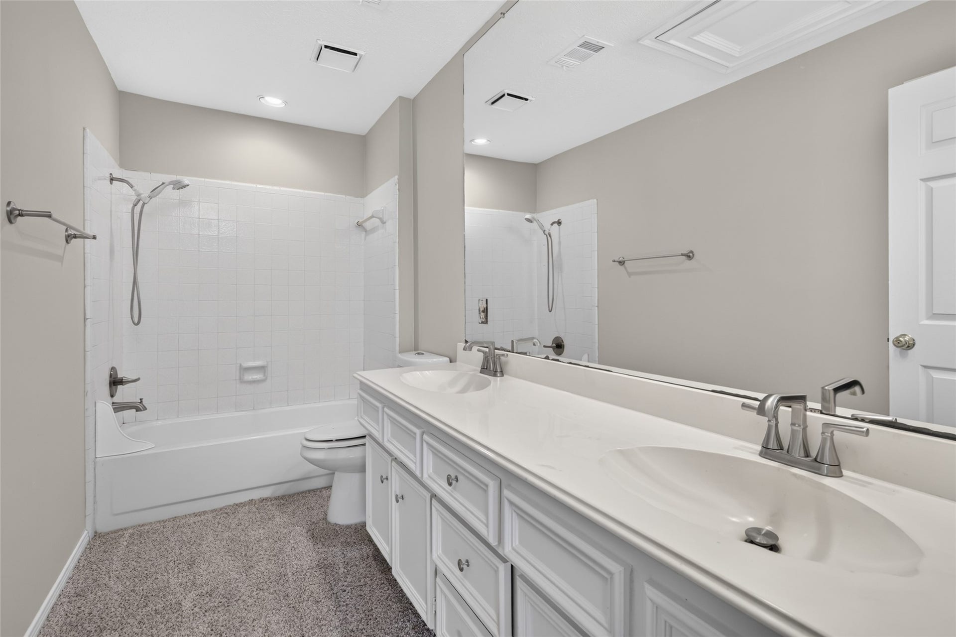 A spacious double vanity, large mirror, and clean white tile surrounding the tub and shower create a bright, functional bathroom designed for everyday convenience.