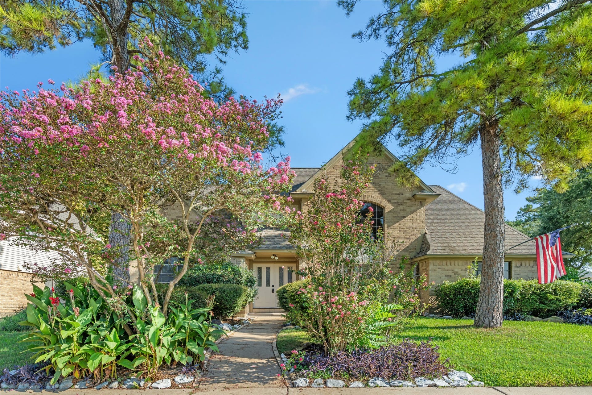 A welcoming approach surrounded by lush greenery and flowering trees creates a serene setting that immediately feels private, established, and ready to call home.