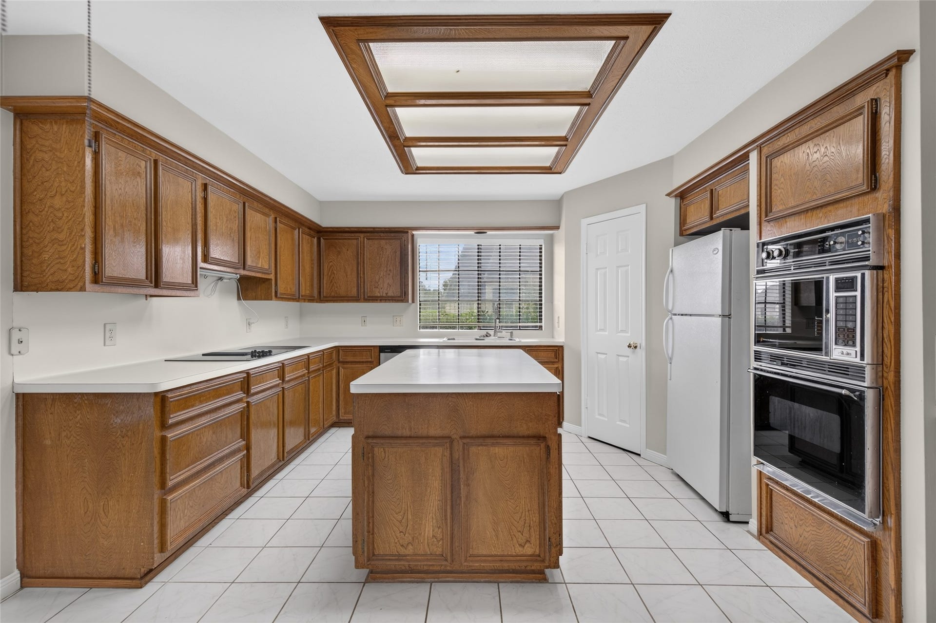 Rich wood cabinetry, a central island, modern appliances, and a large window combine functionality with warmth, creating a kitchen that feels both practical and inviting.