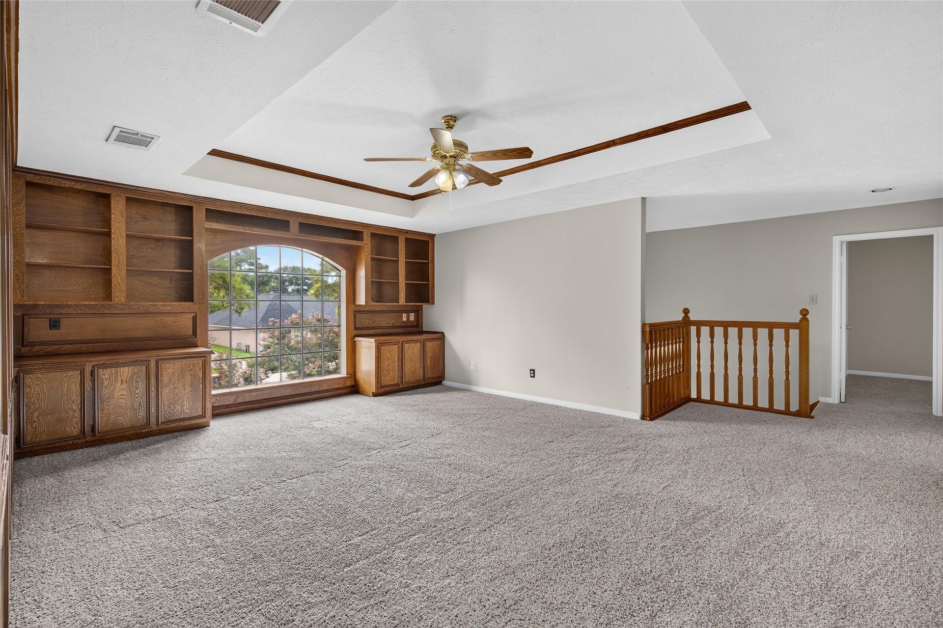 Plush carpeting, built-in wood shelving, and a large arched window create a bright, flexible room with plenty of character and natural light.
