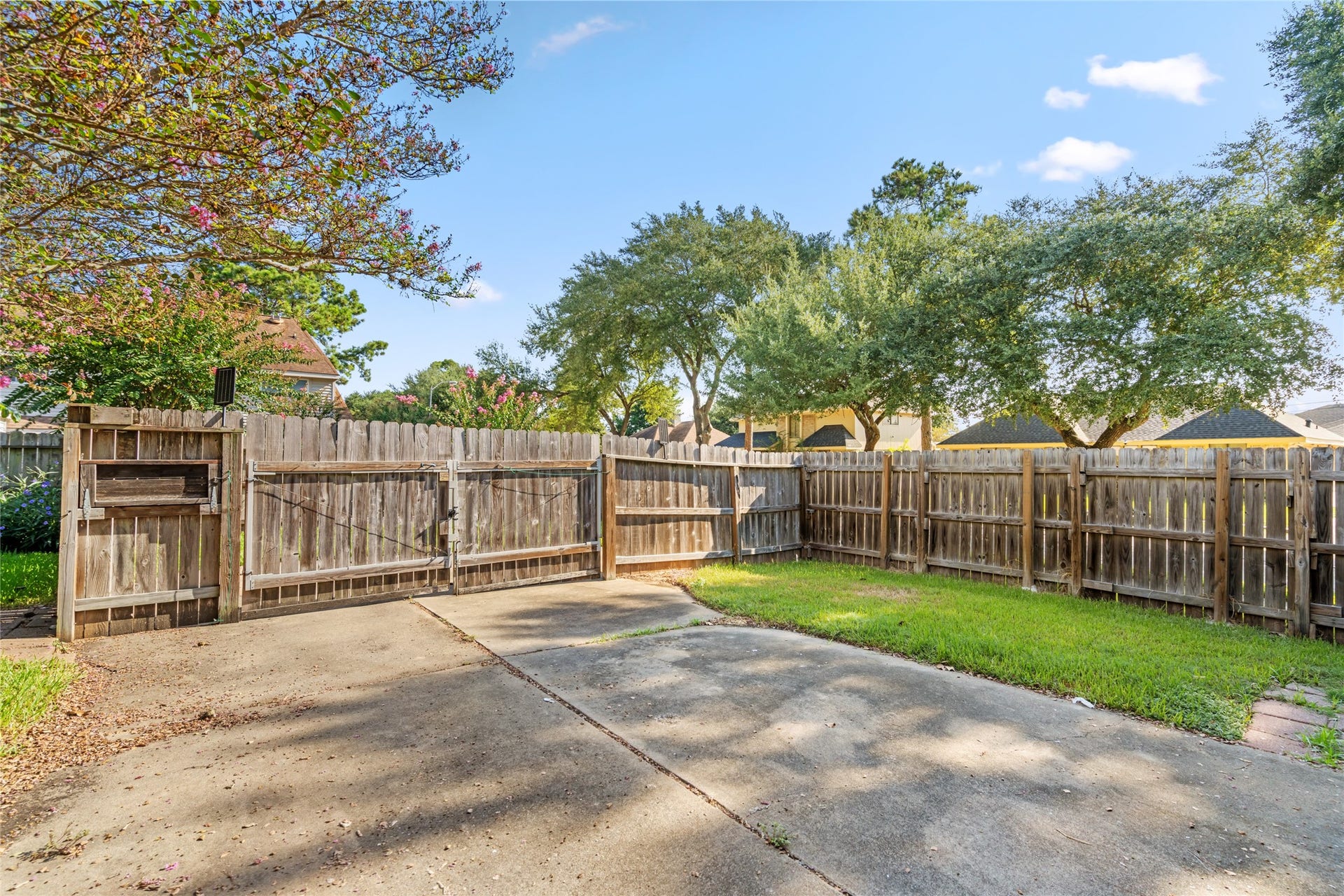 A sturdy wood fence encloses the backyard, creating a private outdoor setting surrounded by mature trees and greenery where buyers can envision relaxing, playing, gardening, or entertaining.