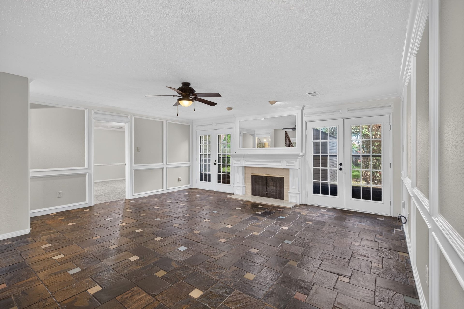 A generous living area combines elegant tile flooring, a cozy fireplace, and French doors leading outdoors, creating a natural setting for entertaining or relaxing while enjoying easy access to the yard.