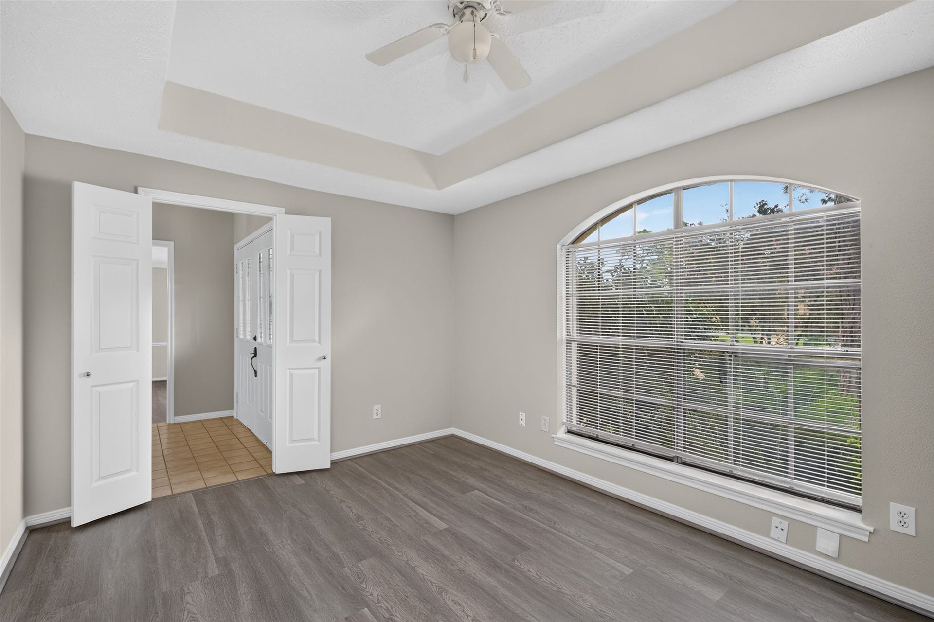 A large arched window fills this room with natural light while the tray ceiling and wood-look flooring add architectural interest, creating a flexible space that can easily become a favorite retreat.